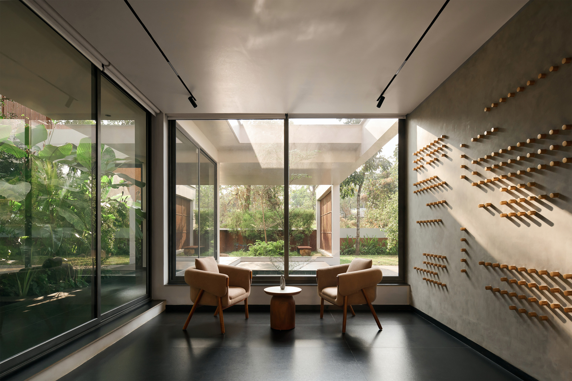 Interior seating alcove with floor-to-ceiling glazing overlooking a planted courtyard and perforated wall panels