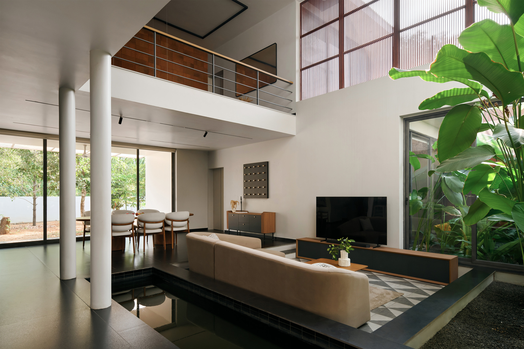 Double-height living room with cylindrical columns, upper mezzanine and a glazed planter with tropical foliage