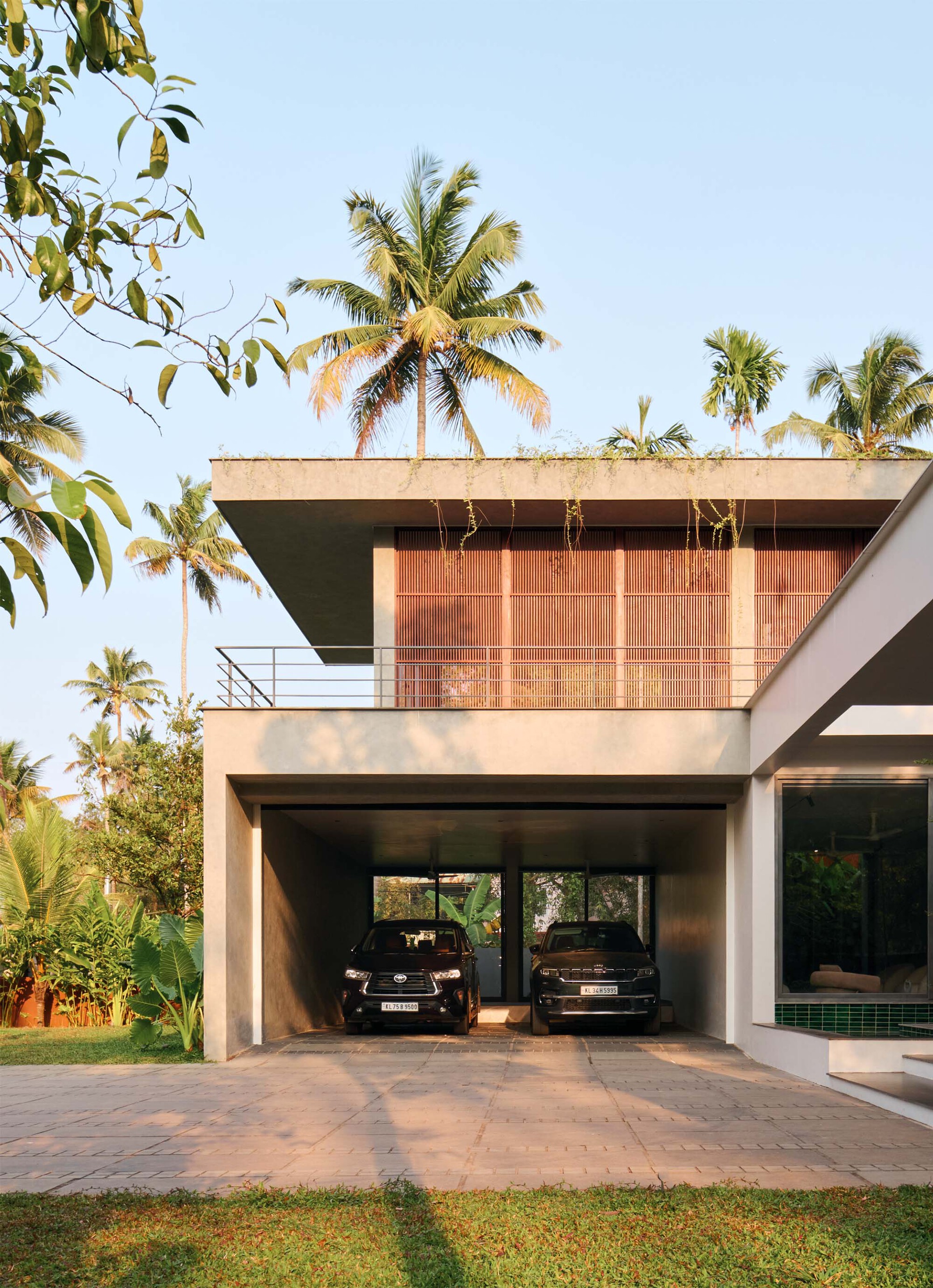 Ground level carport beneath a cantilevered terrace framed by vertical timber screens and palm canopy