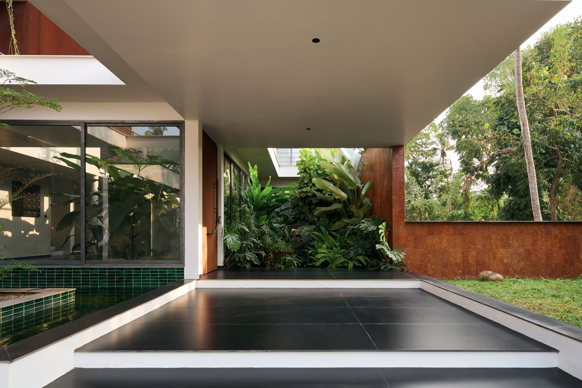 Covered terrace with dark tiled floor adjacent to green tiled pool and vertical garden wall