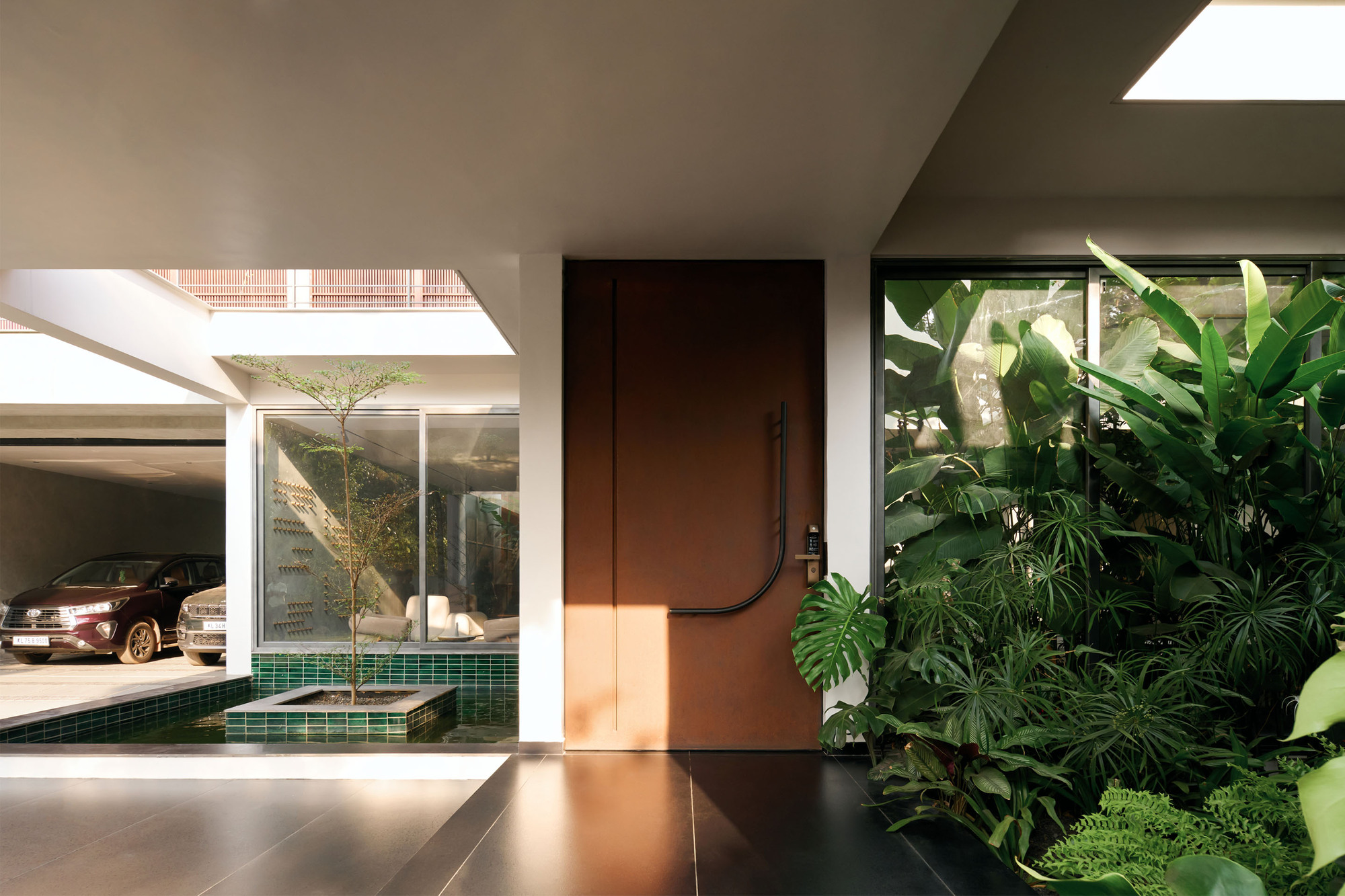 Entry foyer with bronze metal door beside planted courtyard and skylight casting morning shadows