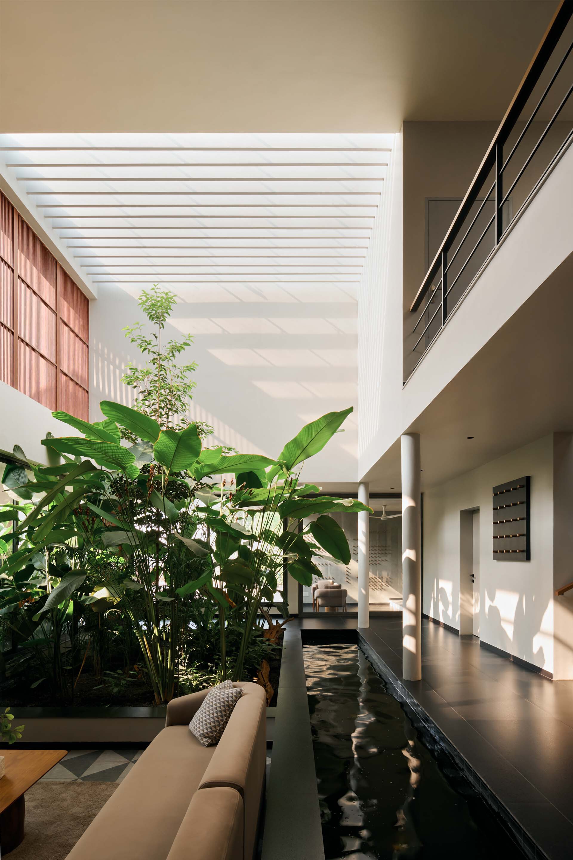 Double-height interior courtyard with reflecting pool, planted banana trees and slatted skylight above