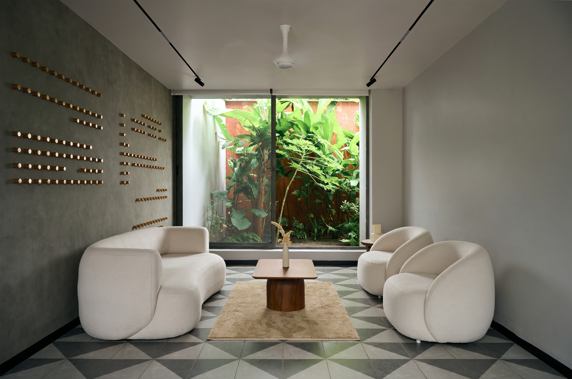 Sitting area with curved sofas and geometric floor tiles facing a window overlooking banana plants