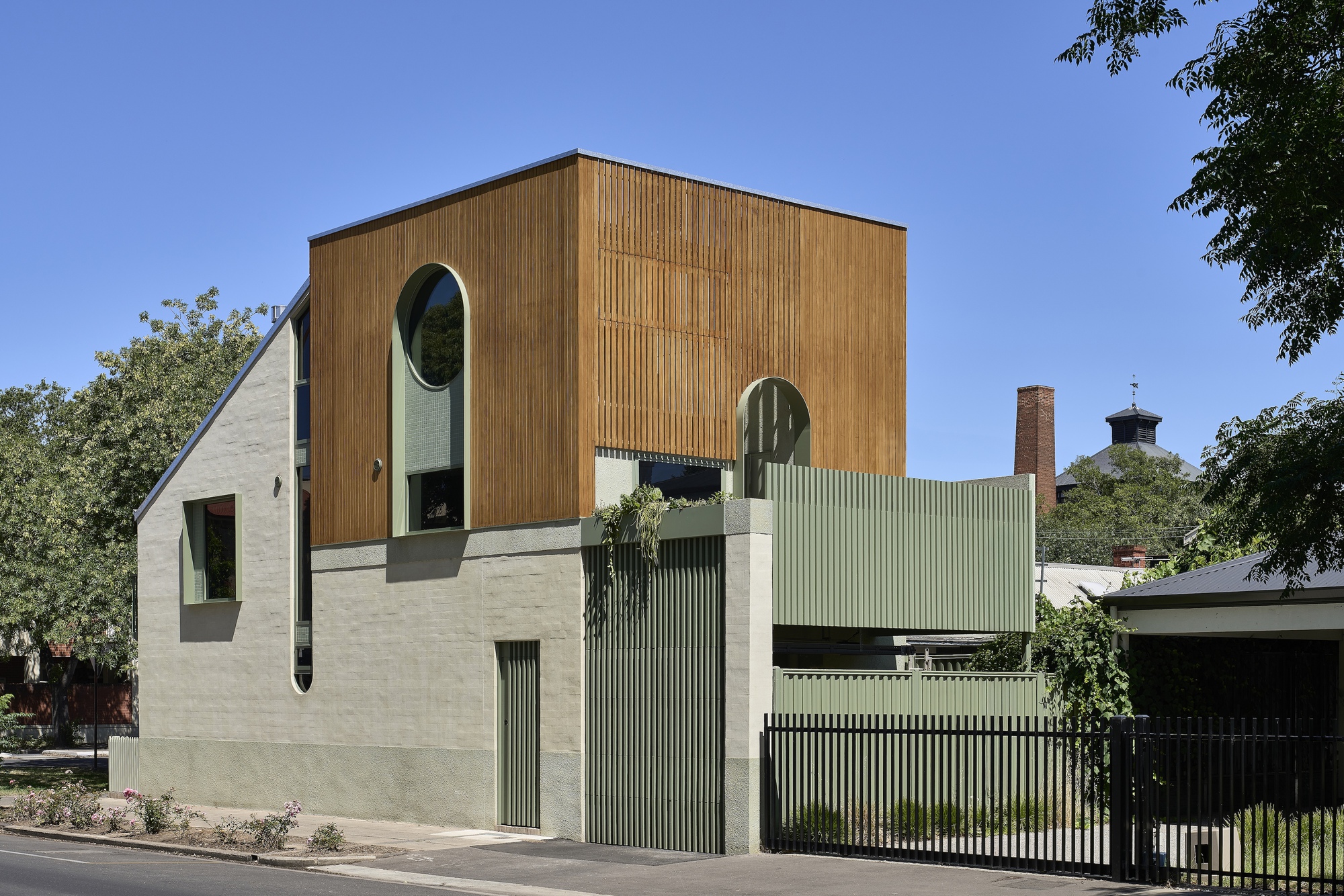 Corner view showing timber box volume above rendered podium with corrugated metal fence and gate