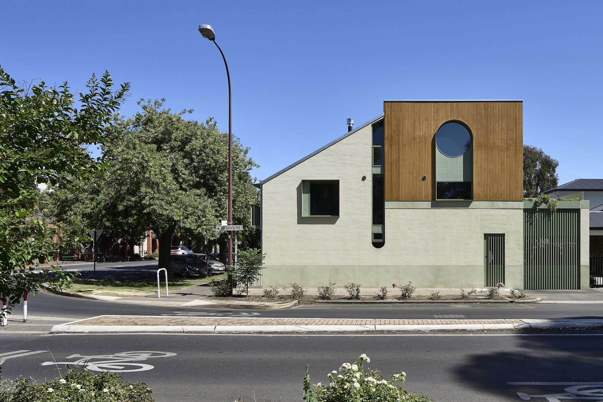 Street view of the two-storey facade with vertical timber cladding and circular window under clear blue sky