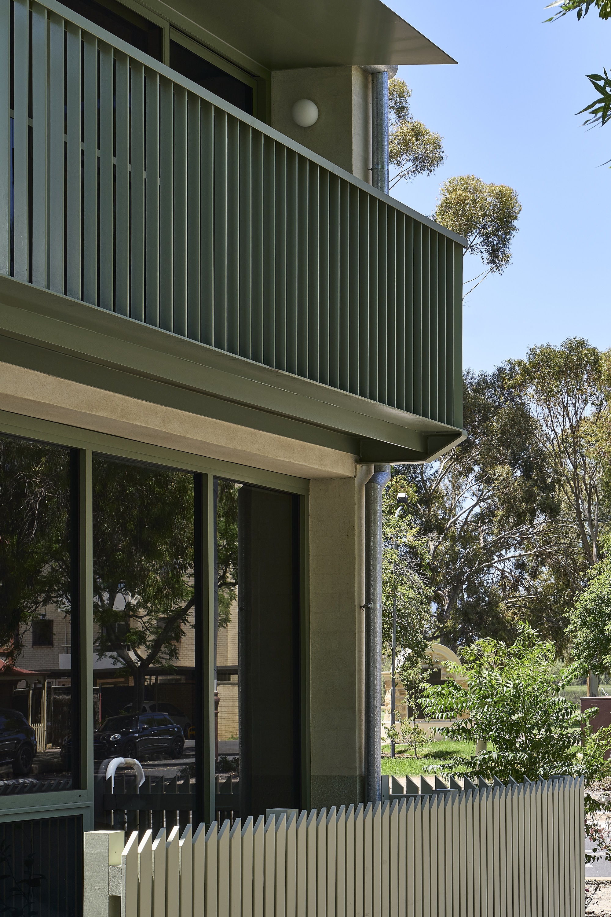 Cantilevered balcony with vertical green metal slat screen above full-height glazed doors