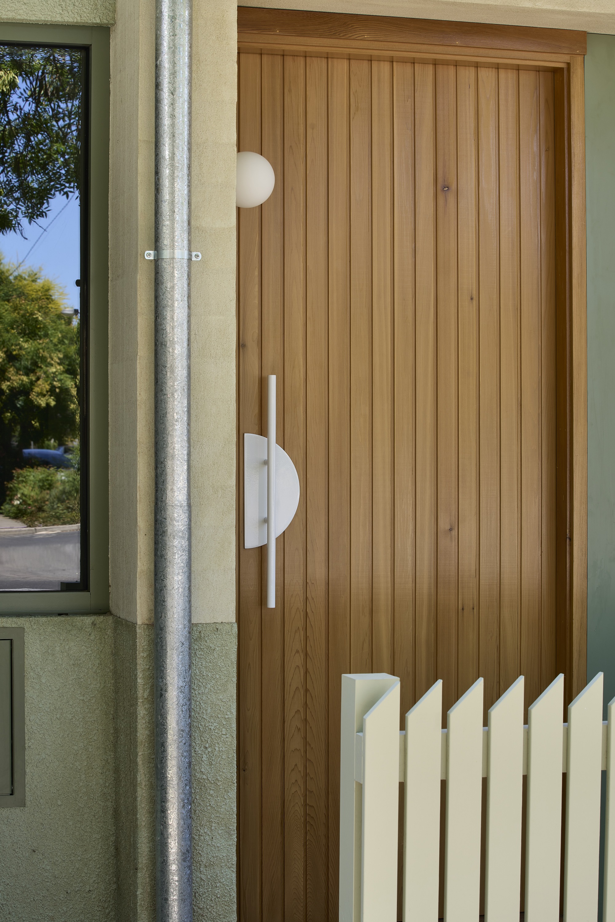 Vertical timber-clad entry door with white semicircular handle and adjacent concrete downpipe