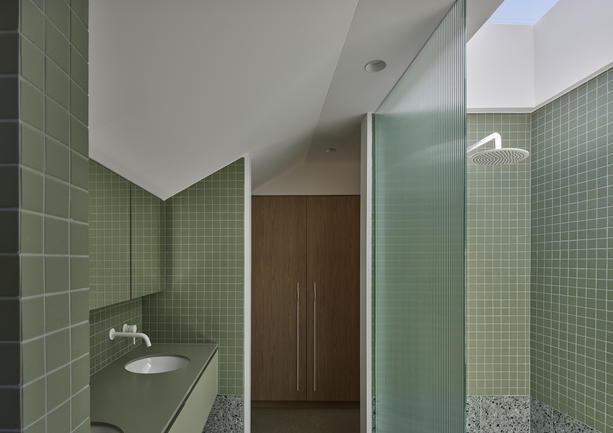 Bathroom interior with green square tile walls, fluted glass shower screen and terrazzo flooring