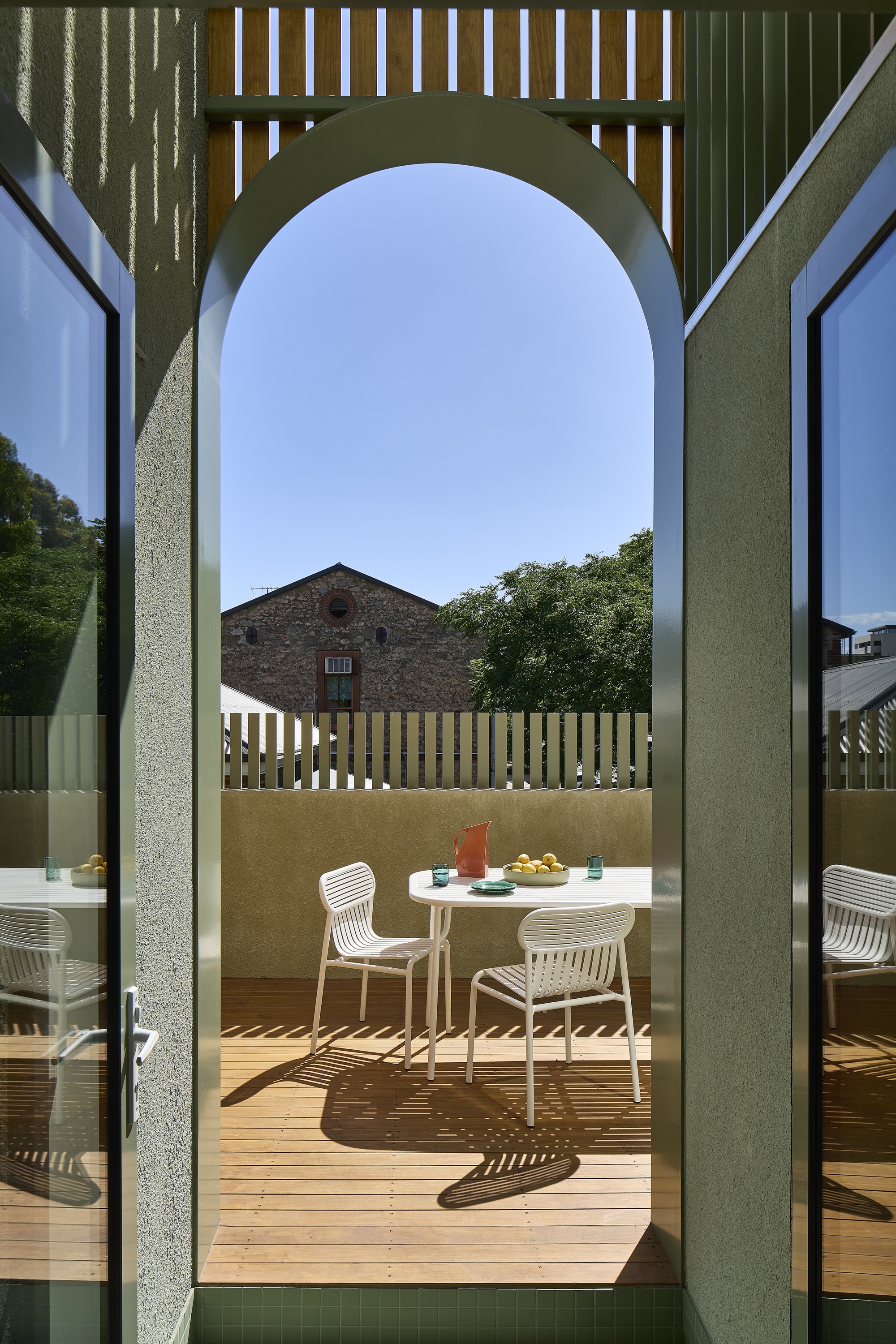 Arched doorway framing timber deck terrace with dining furniture and vertical slat screening