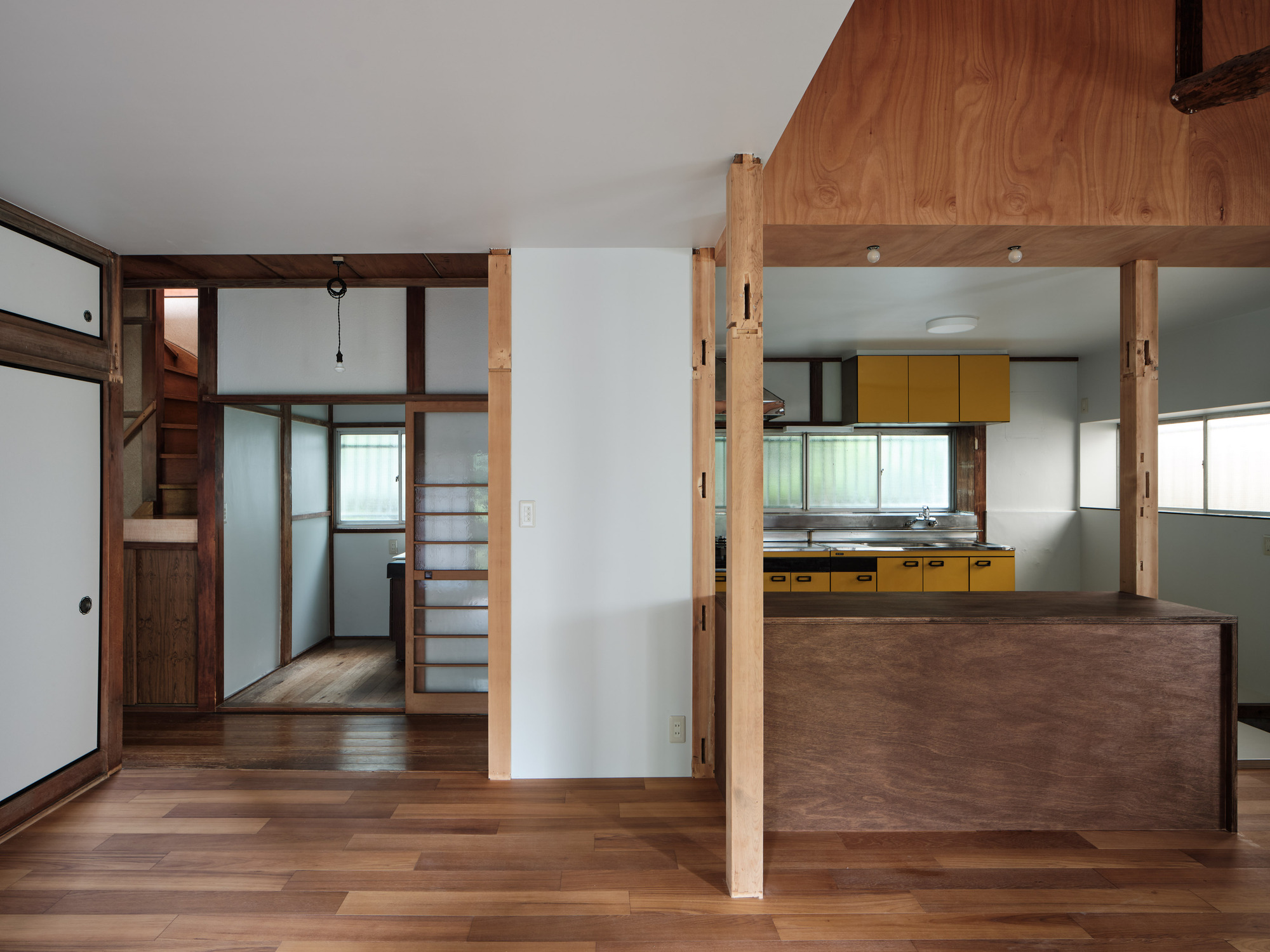 View through timber columns toward yellow kitchen cabinetry and translucent sliding screens on the left