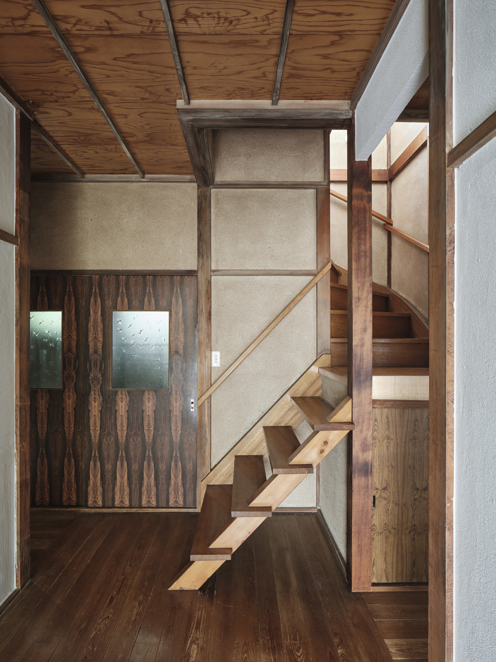 Open timber staircase rising against a textured plaster wall beneath an exposed beam ceiling