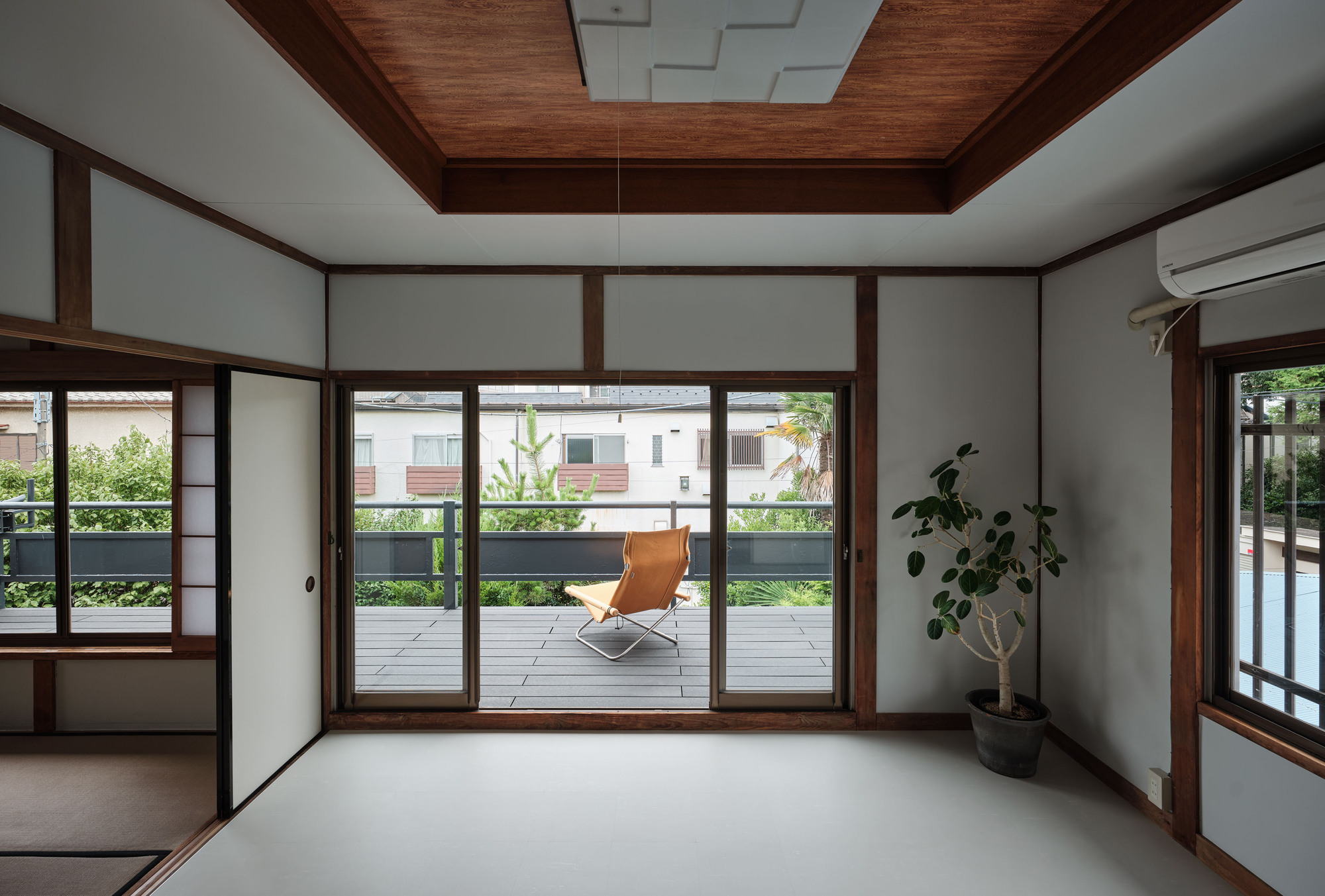 Interior room with timber-framed sliding doors opening onto a terrace with a single chair and potted plant