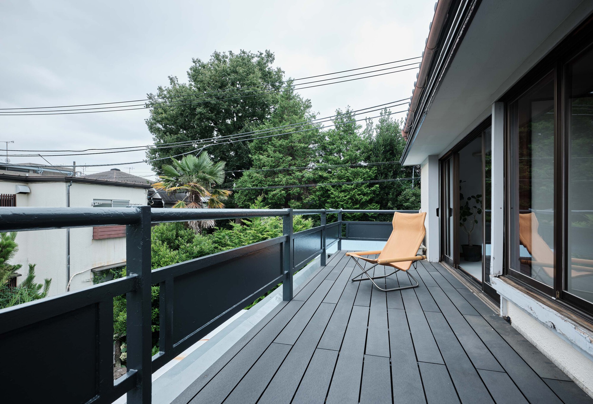 Timber deck terrace with dark metal railings and a single lounge chair facing treetops under overcast sky