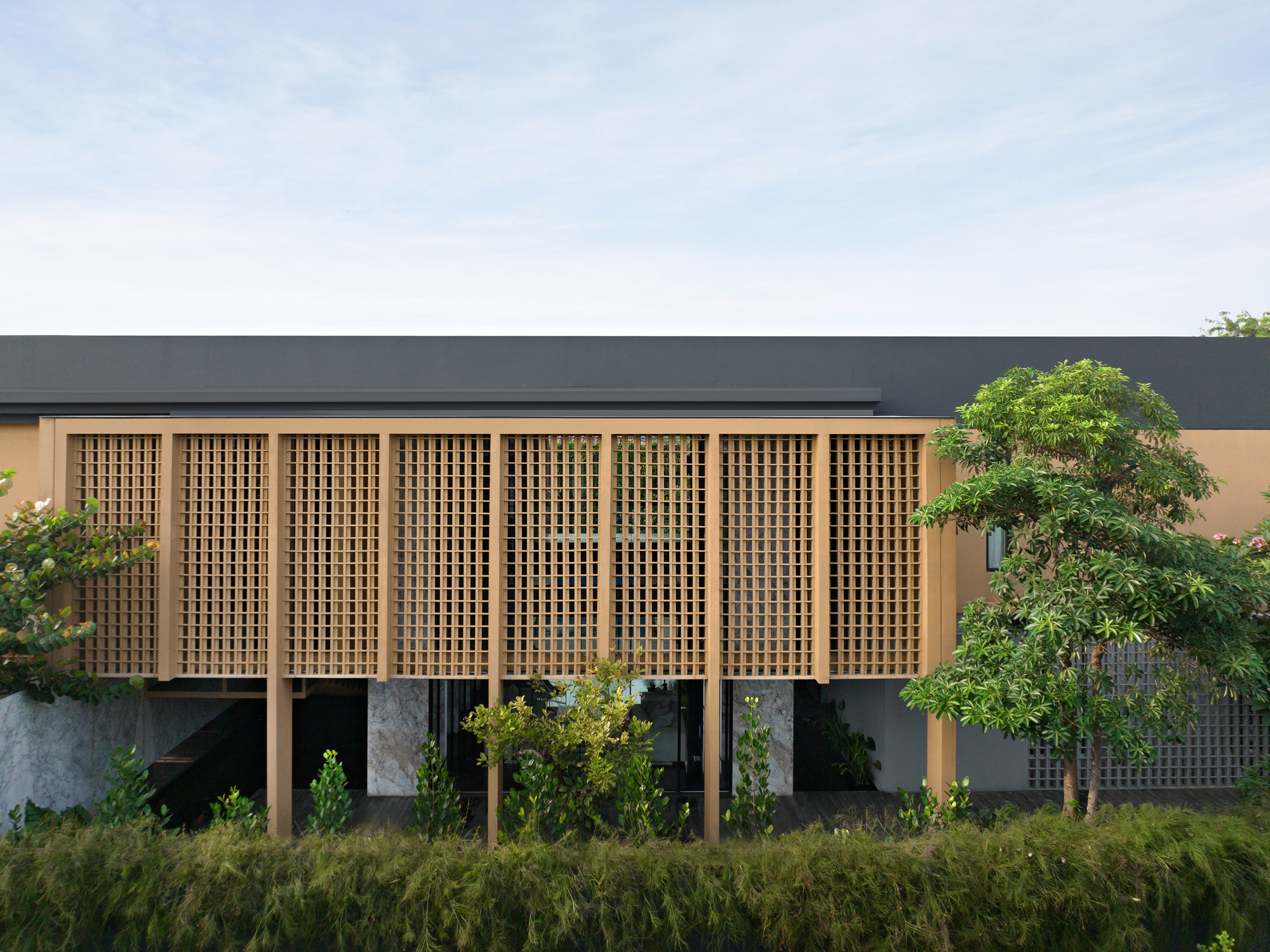 Timber lattice screen facade elevated on columns with grasses and trees in the foreground