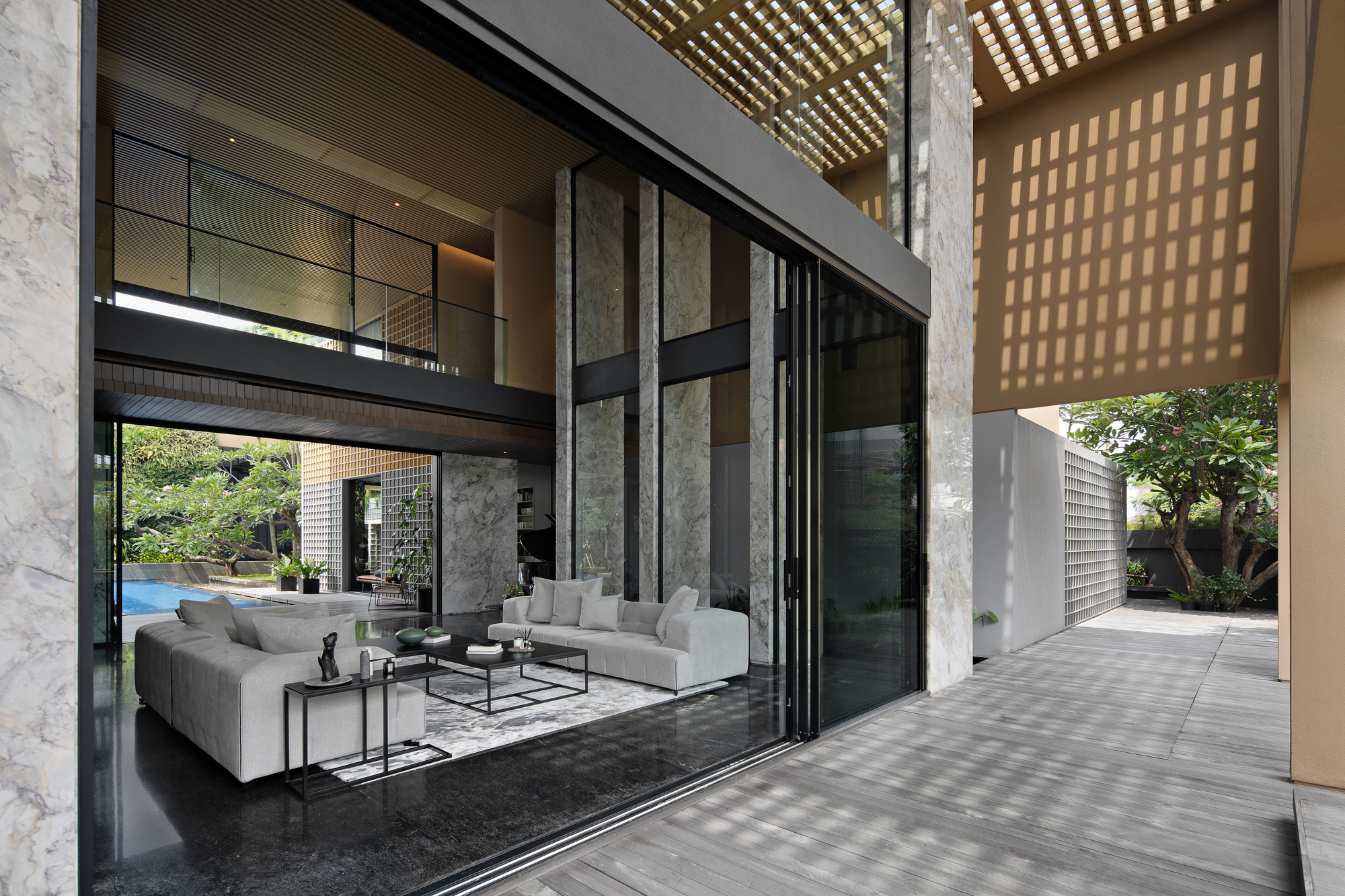 View from covered outdoor terrace through sliding glass doors into the living room with mezzanine and pool beyond