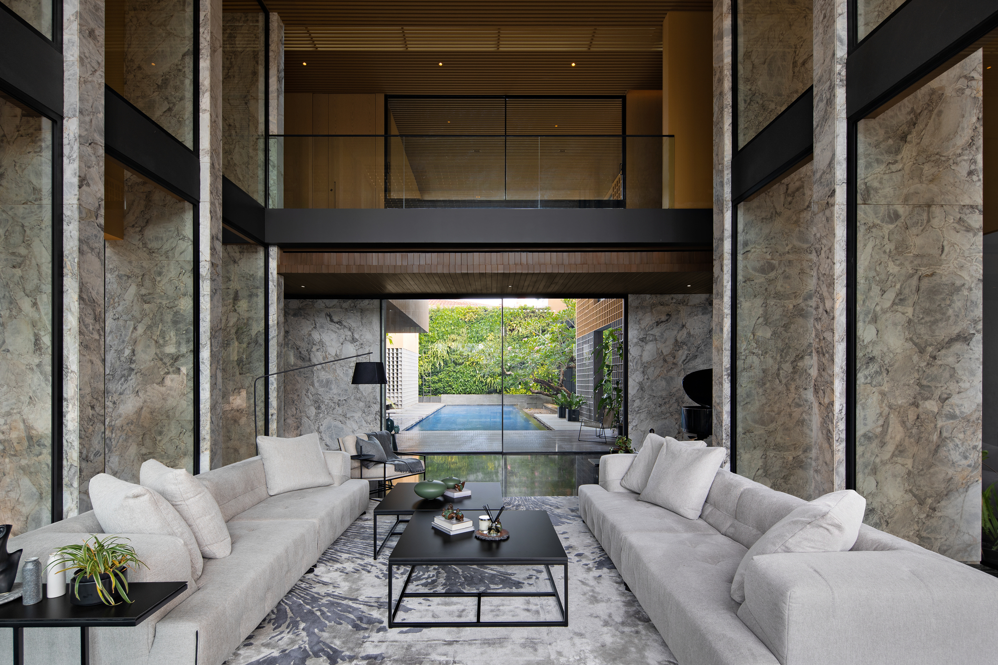 Axial view through the living space toward the pool courtyard framed by mezzanine bridge and stone columns