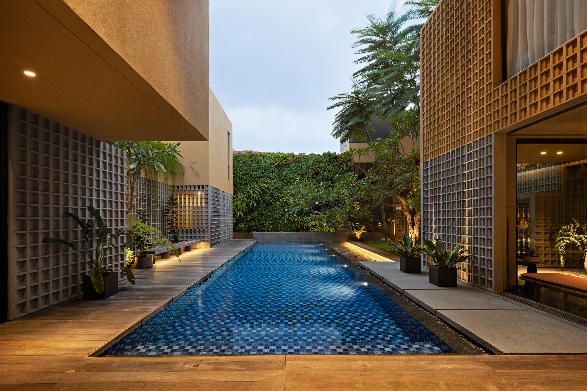 Blue mosaic tile pool flanked by timber decking and perforated concrete block walls at twilight