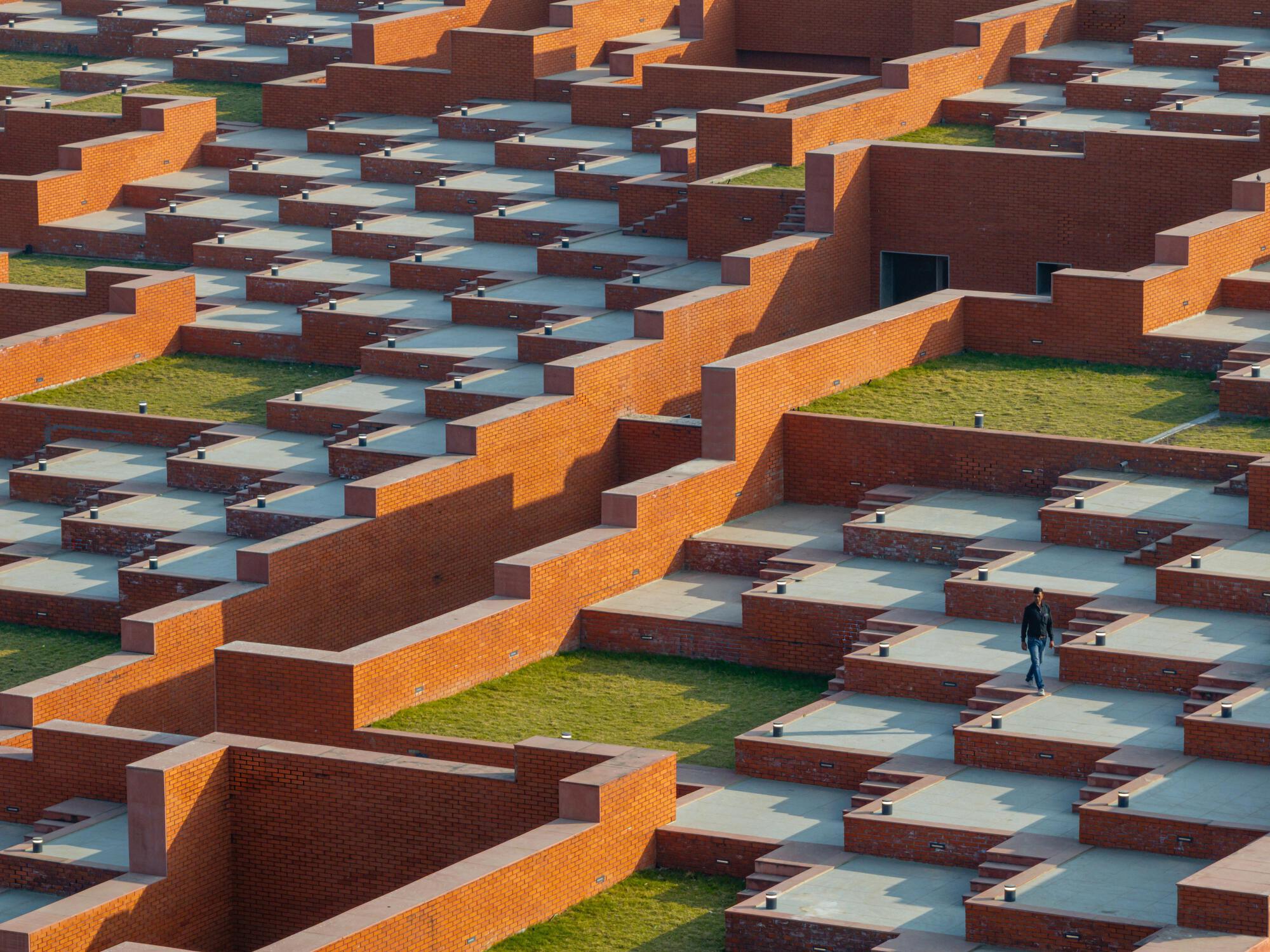 Overhead view of stepped brick terraces with grass courtyards and a solitary figure walking below