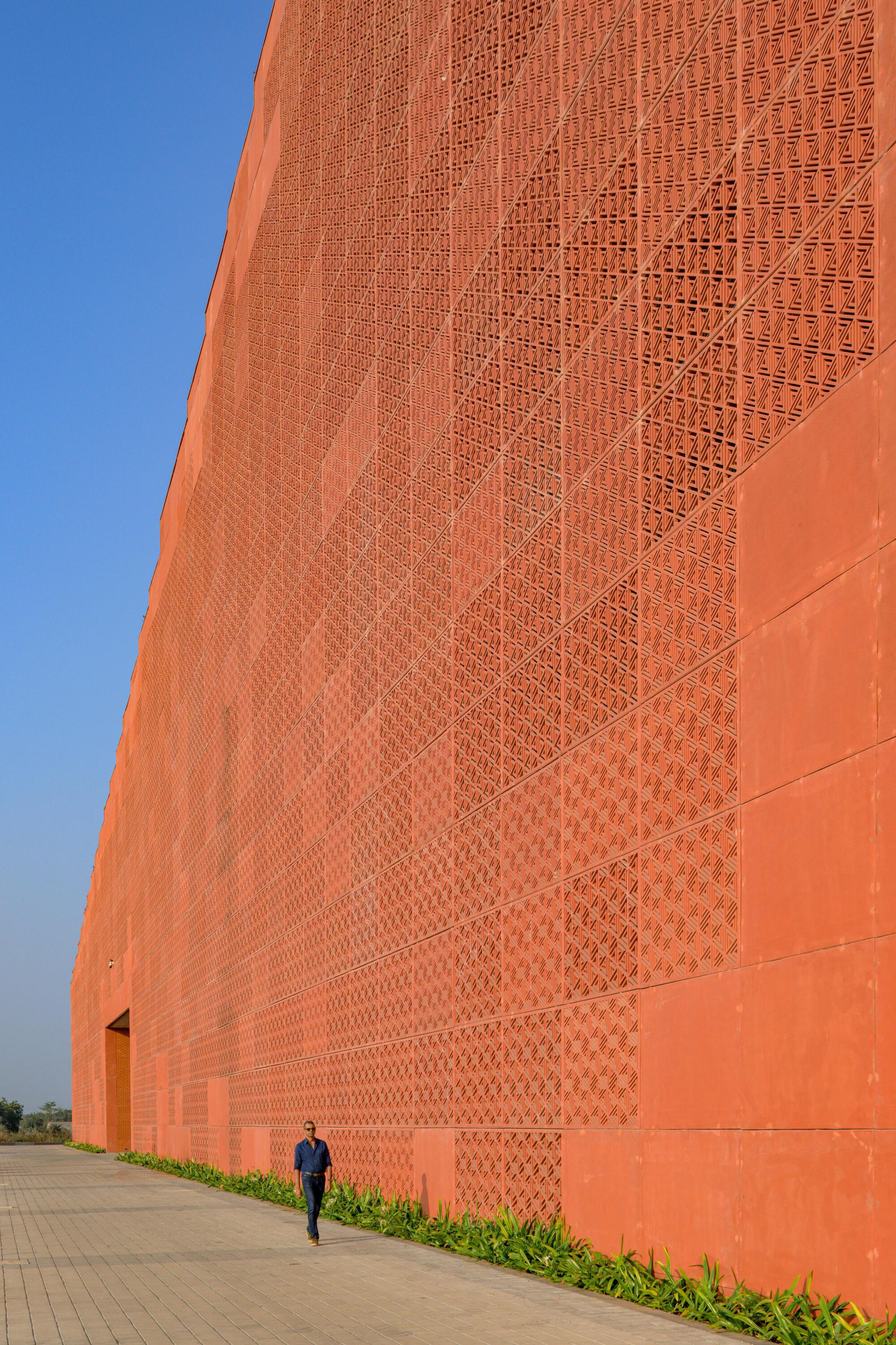 Close-up of orange brick wall with patterned perforations and a figure walking along the paved edge
