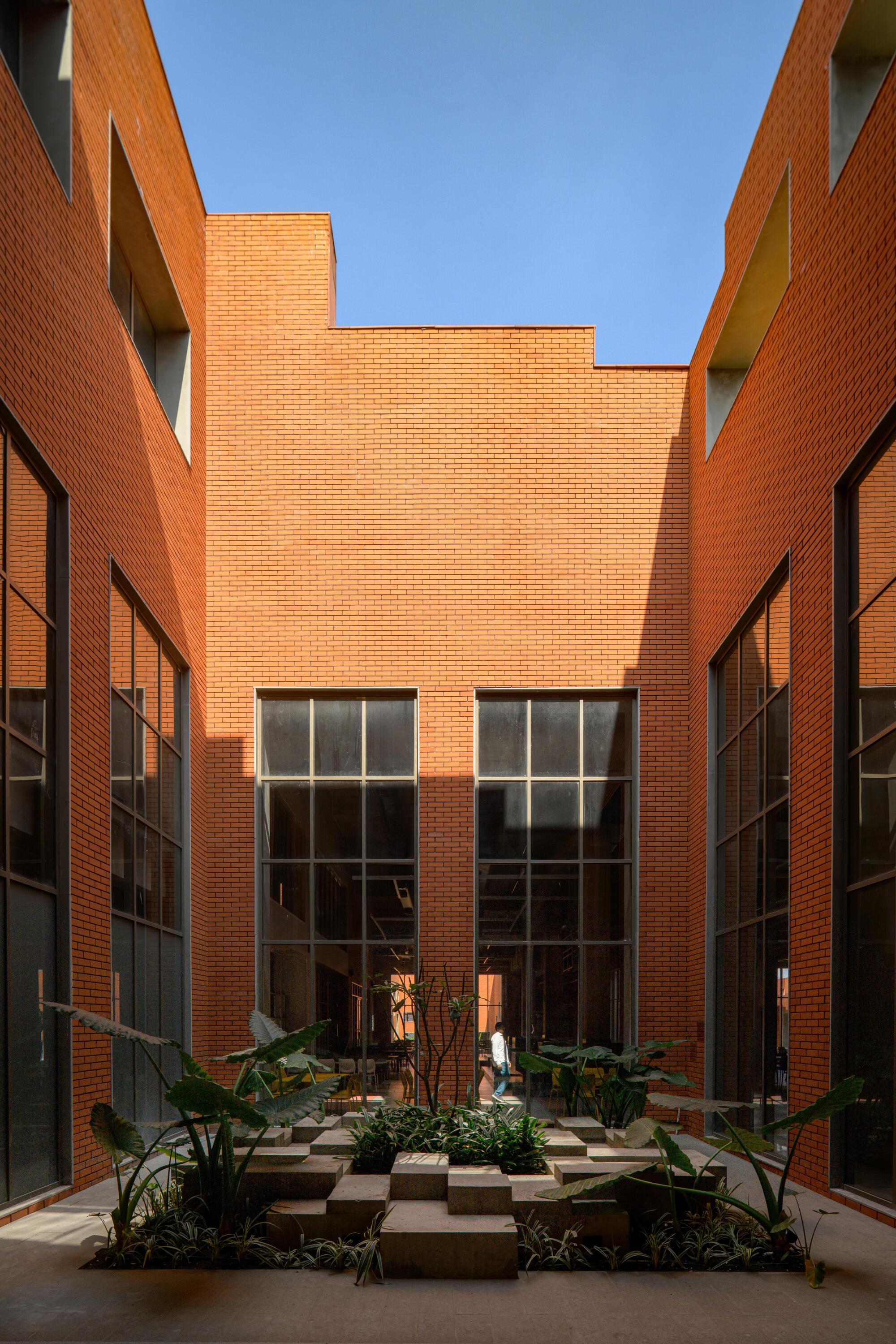 Narrow courtyard passage with tall brick walls and large gridded windows under bright midday sun