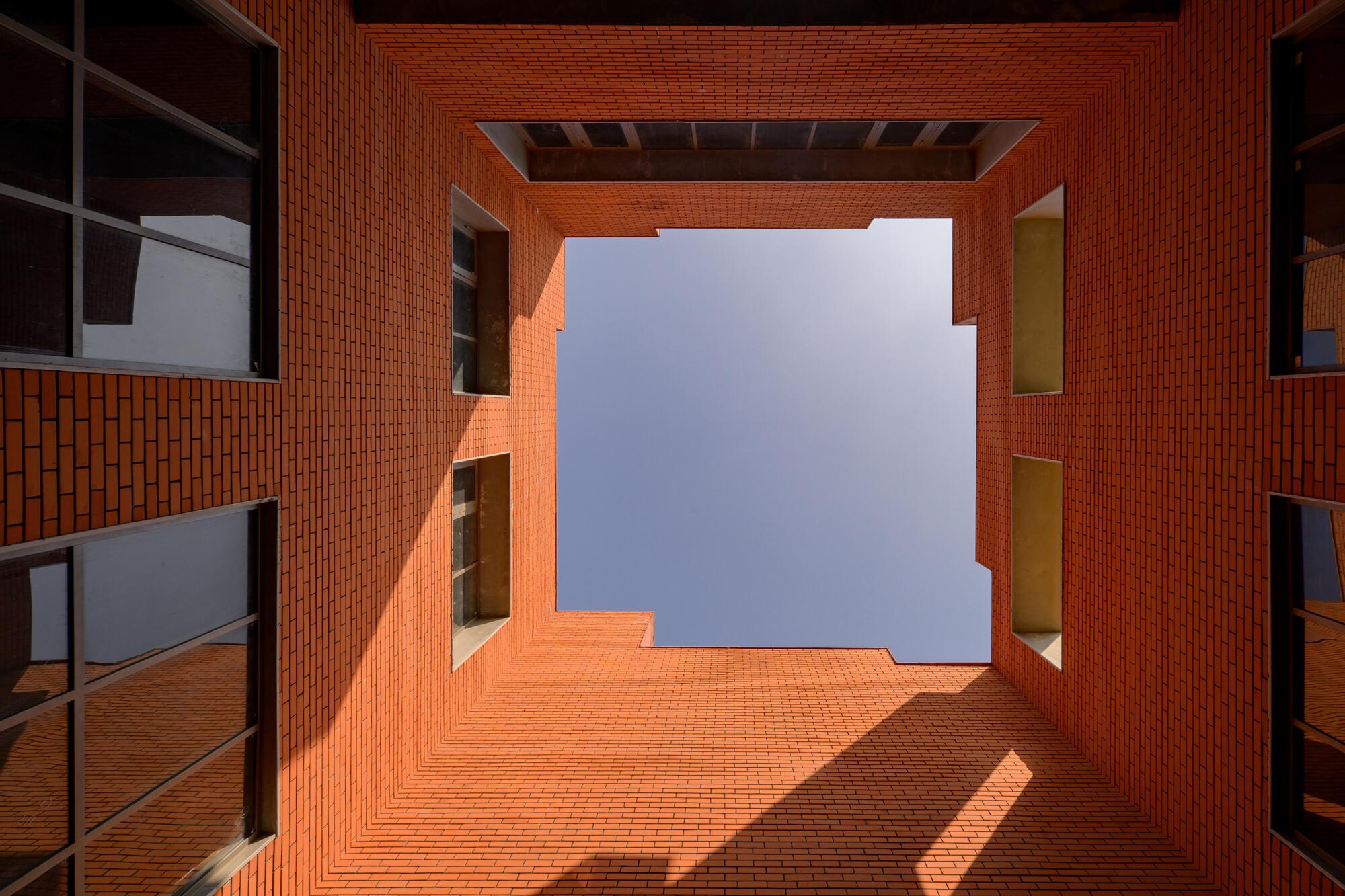 Upward view through a rectangular courtyard framed by orange brick walls and punched window openings