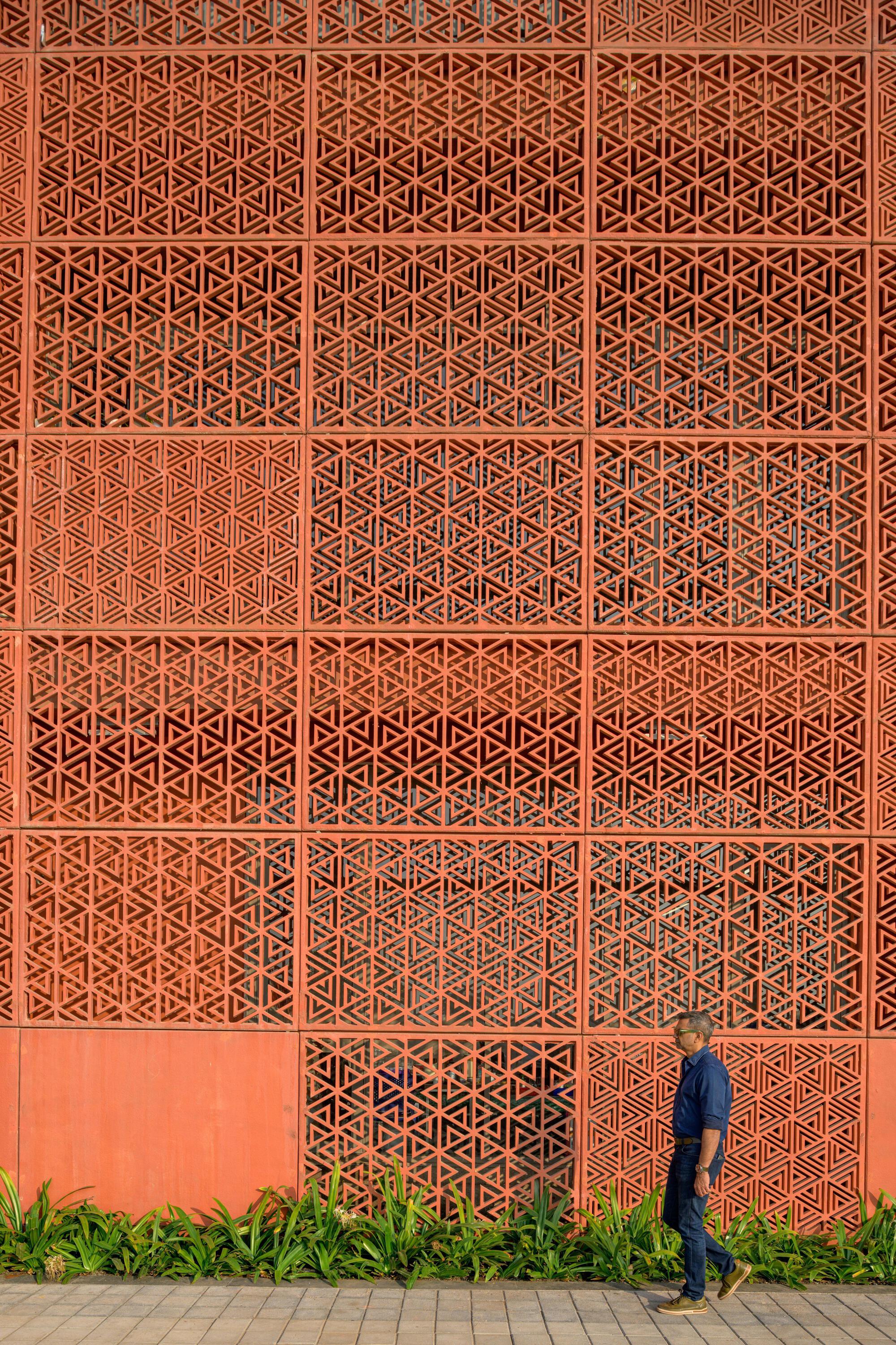 Perforated terracotta brick screen wall with geometric patterning beside a pedestrian walking path