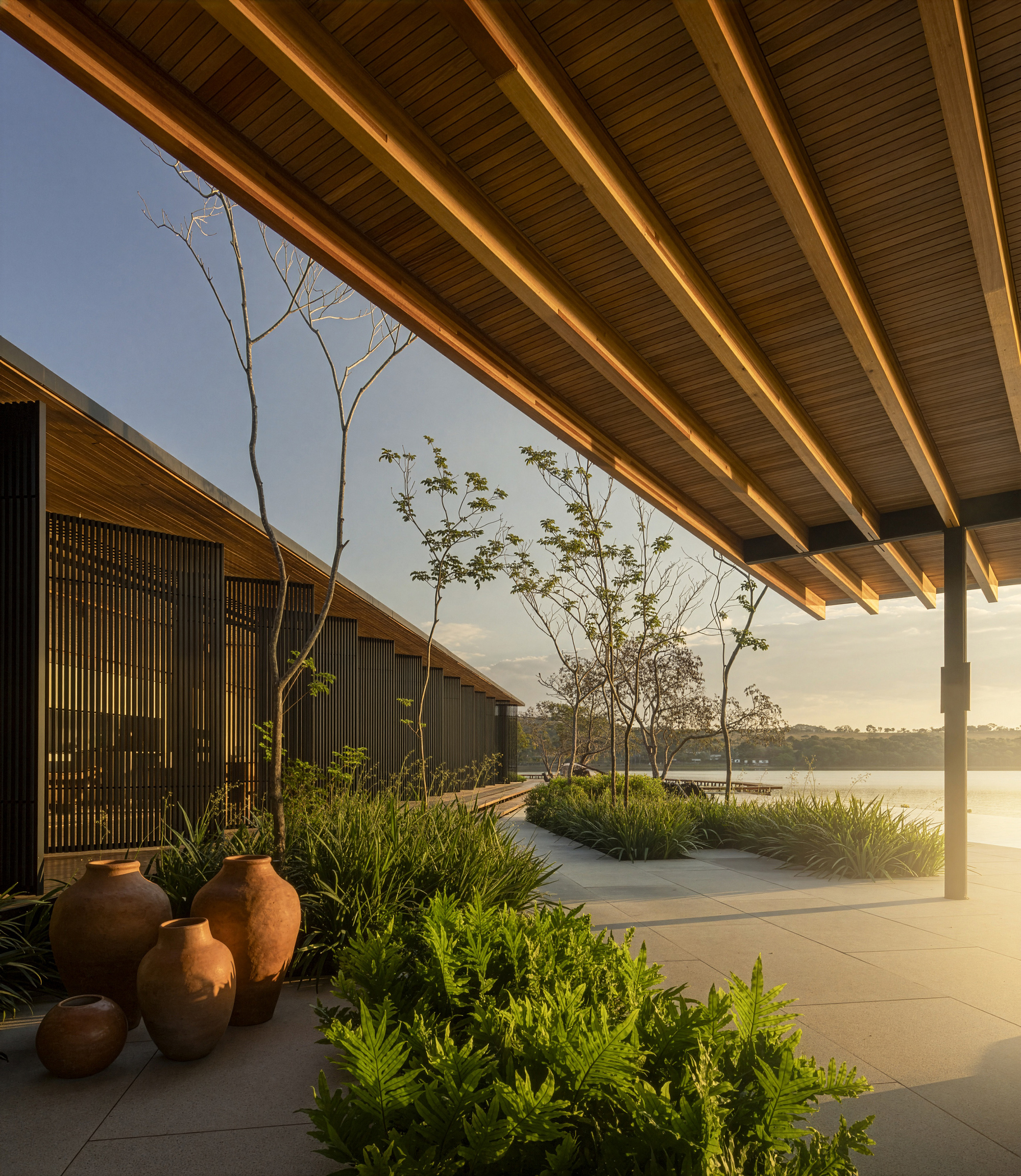 Covered terrace with exposed timber beams and planted beds overlooking the lake at sunset