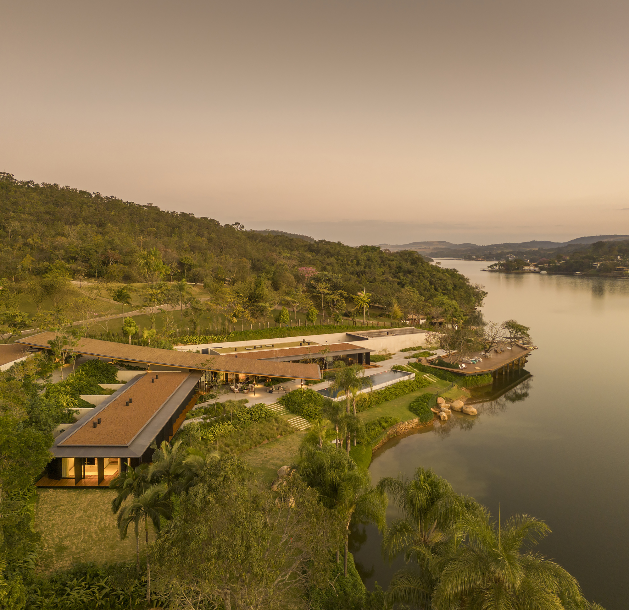 Aerial view of the low-slung roof volumes nestled into the lakeside hillside at dusk
