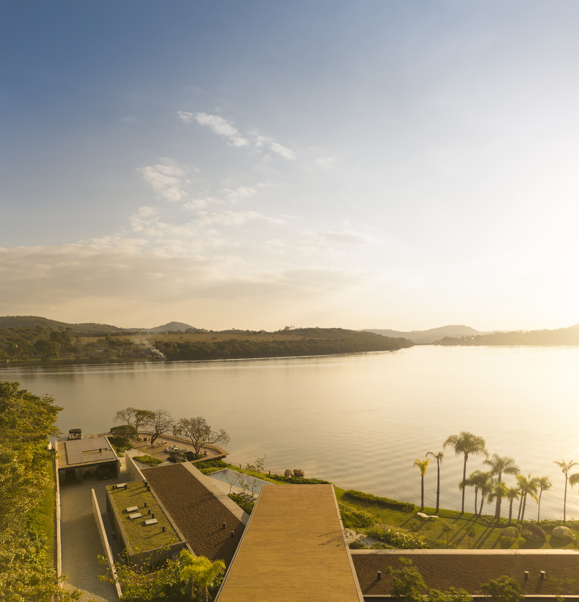 Aerial view of the lakeside terrace and sloped roof planes at sunset with palm trees below