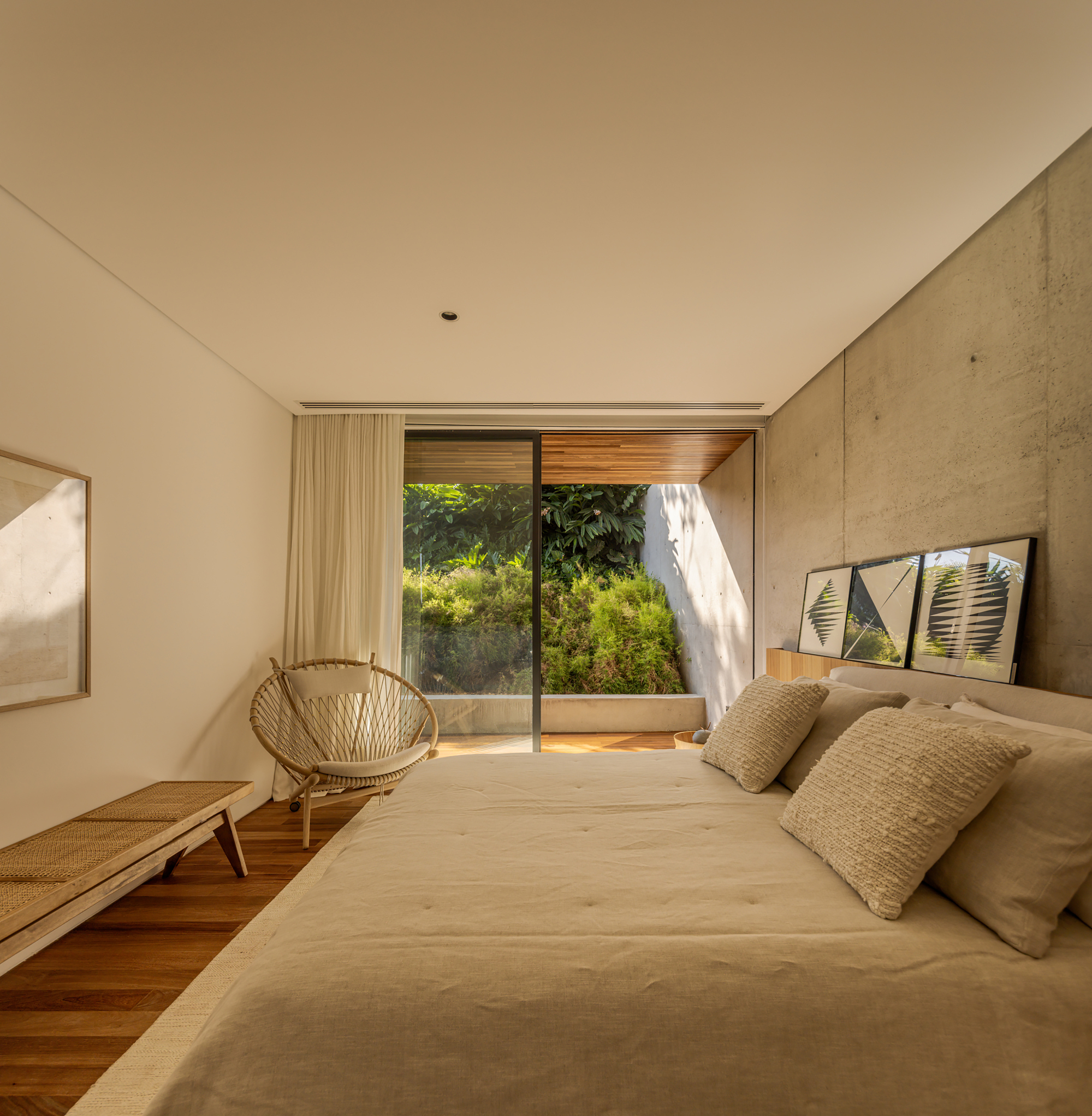 Bedroom with concrete accent wall and glass doors opening to a planted terrace with morning sunlight