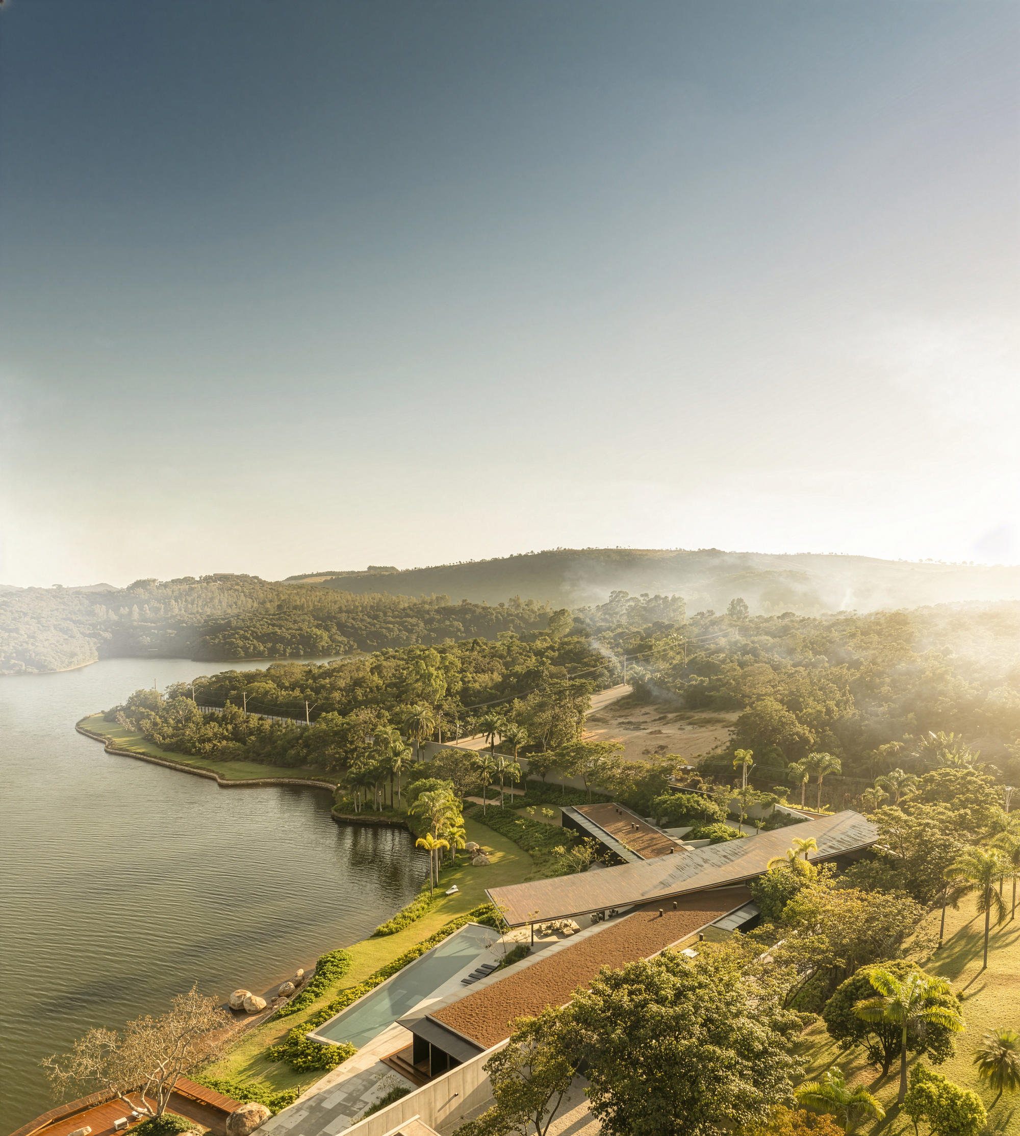 Aerial view of the low-slung residence with sweeping roofline along a forested peninsula at golden hour