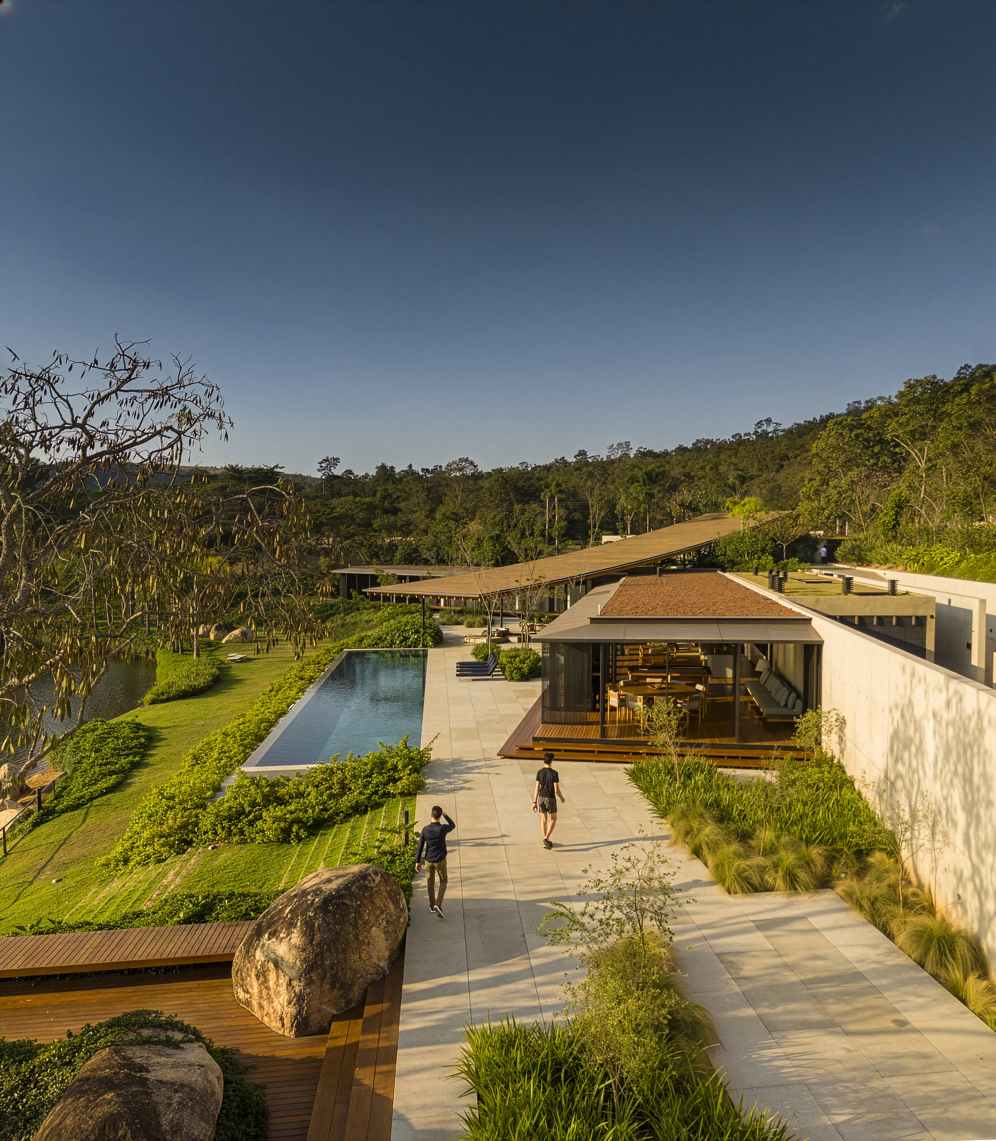 Stone courtyard with rectangular pool and figures walking between pavilions in late afternoon light