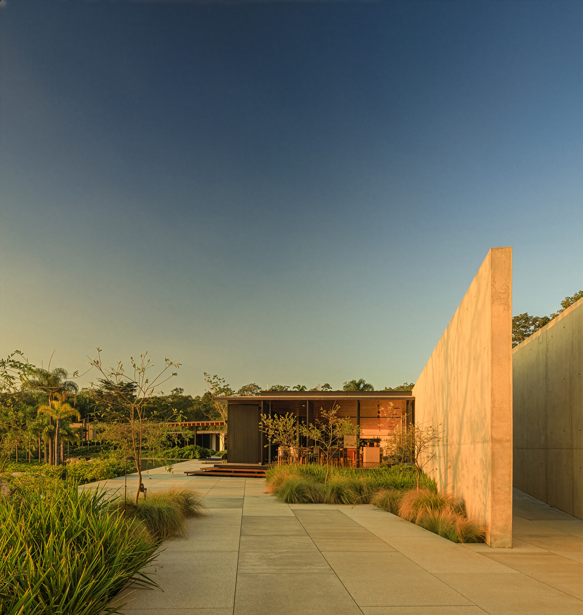 Concrete walkway flanked by planted beds leading toward timber pavilion at sunset