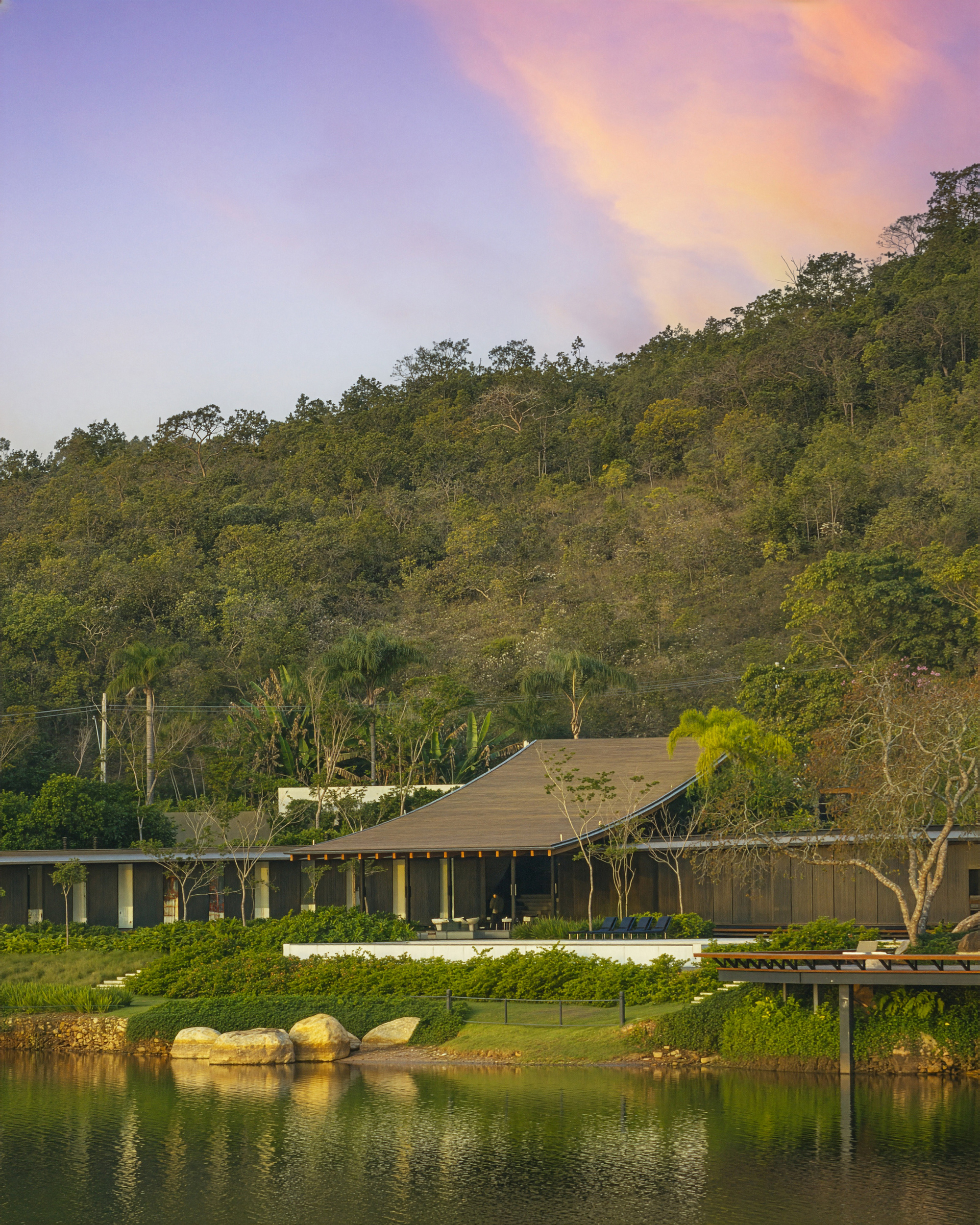 Lakeside view of the timber-roofed pavilion beneath a forested hillside at dusk