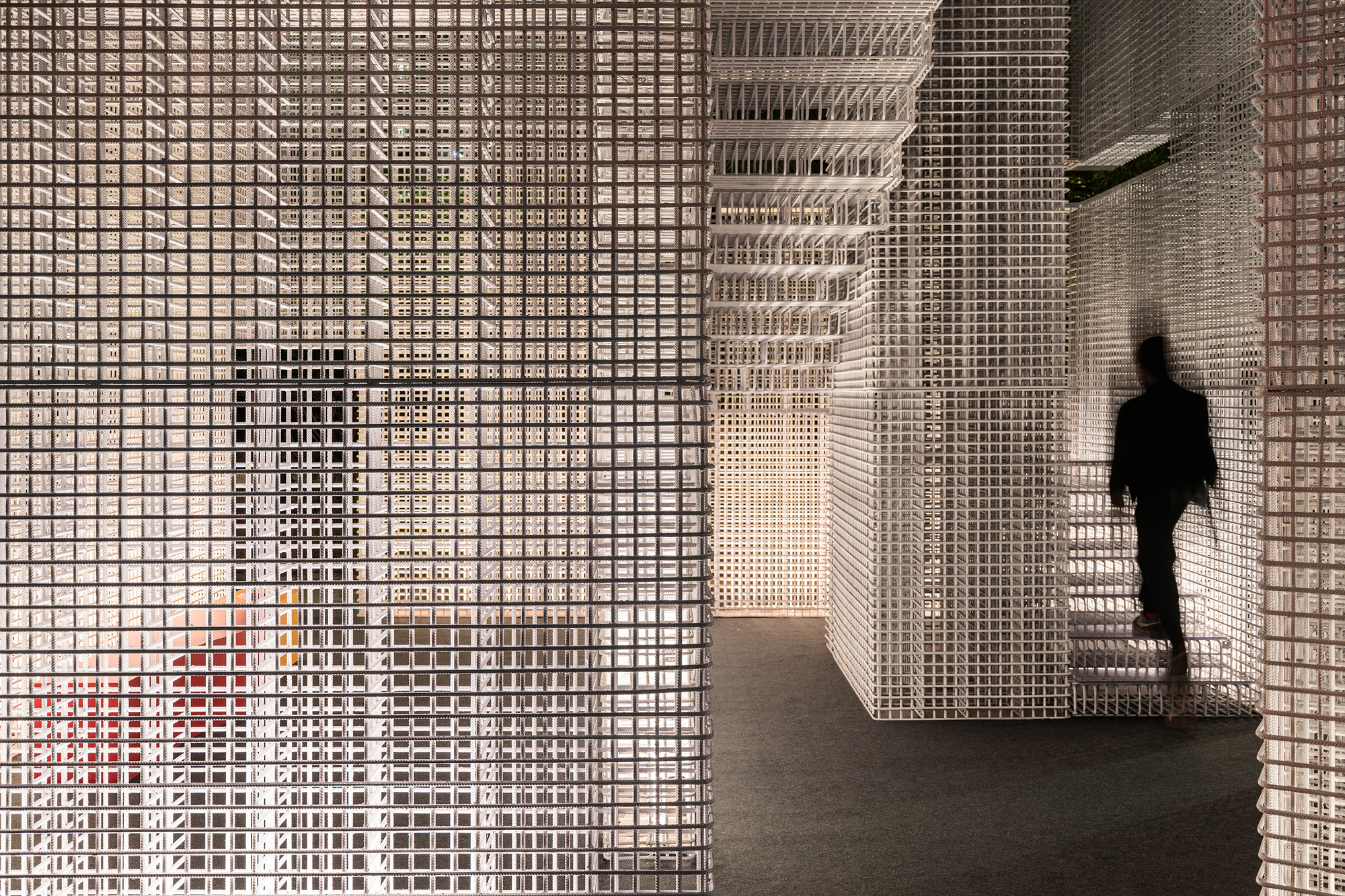 Interior corridor with white perforated mesh walls and ceiling as a figure walks past in shadow