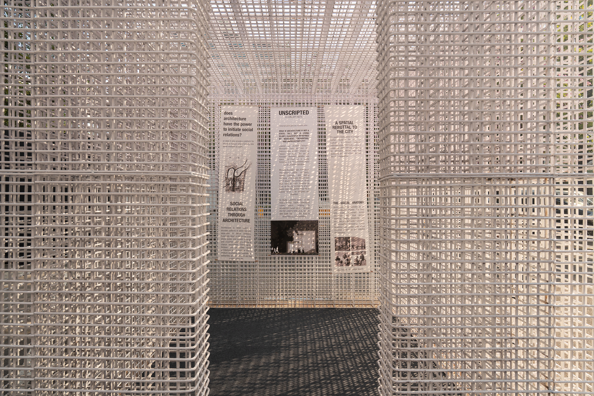White grid screen enclosure with exhibition panels mounted on the rear wall beneath a perforated ceiling