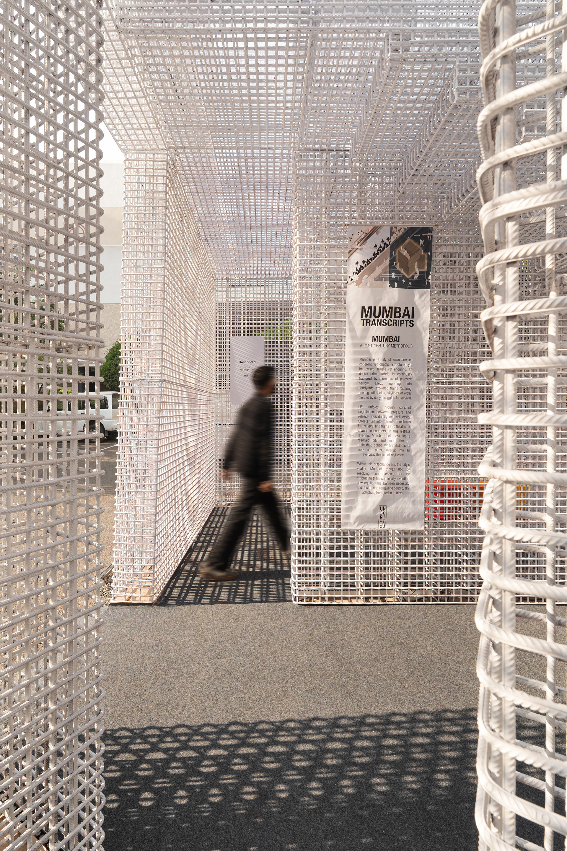 Passageway through white lattice walls with a blurred visitor walking past informational displays and cylindrical column