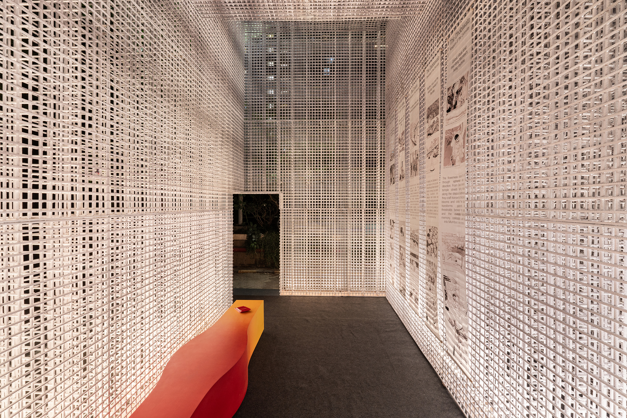 Narrow corridor enclosed by white perforated mesh screens with an orange bench and dark carpet flooring