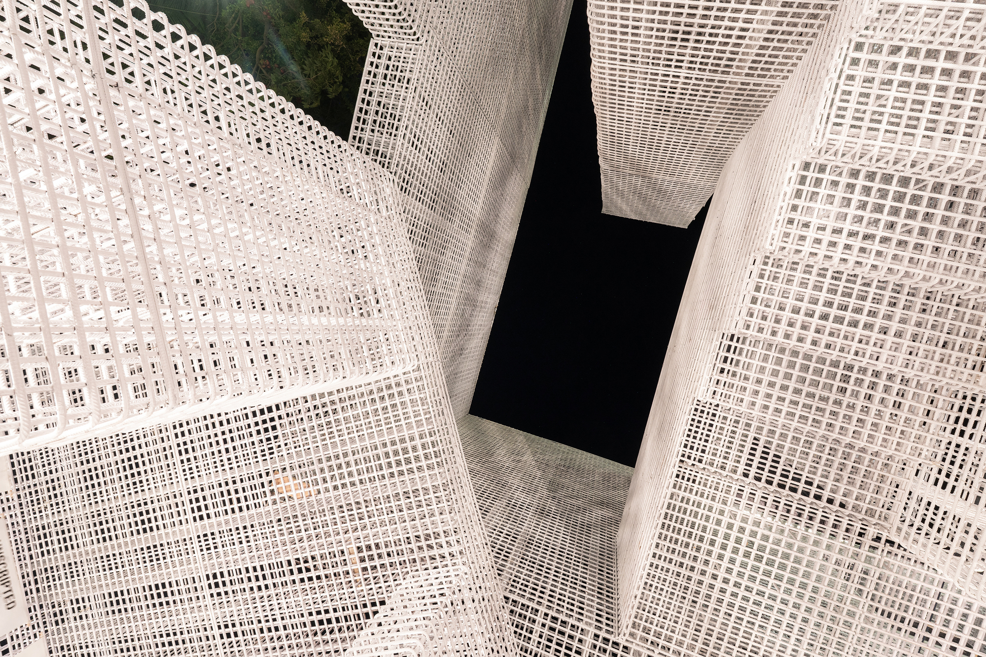 Looking up through white mesh-wrapped volumes intersecting around a dark central void
