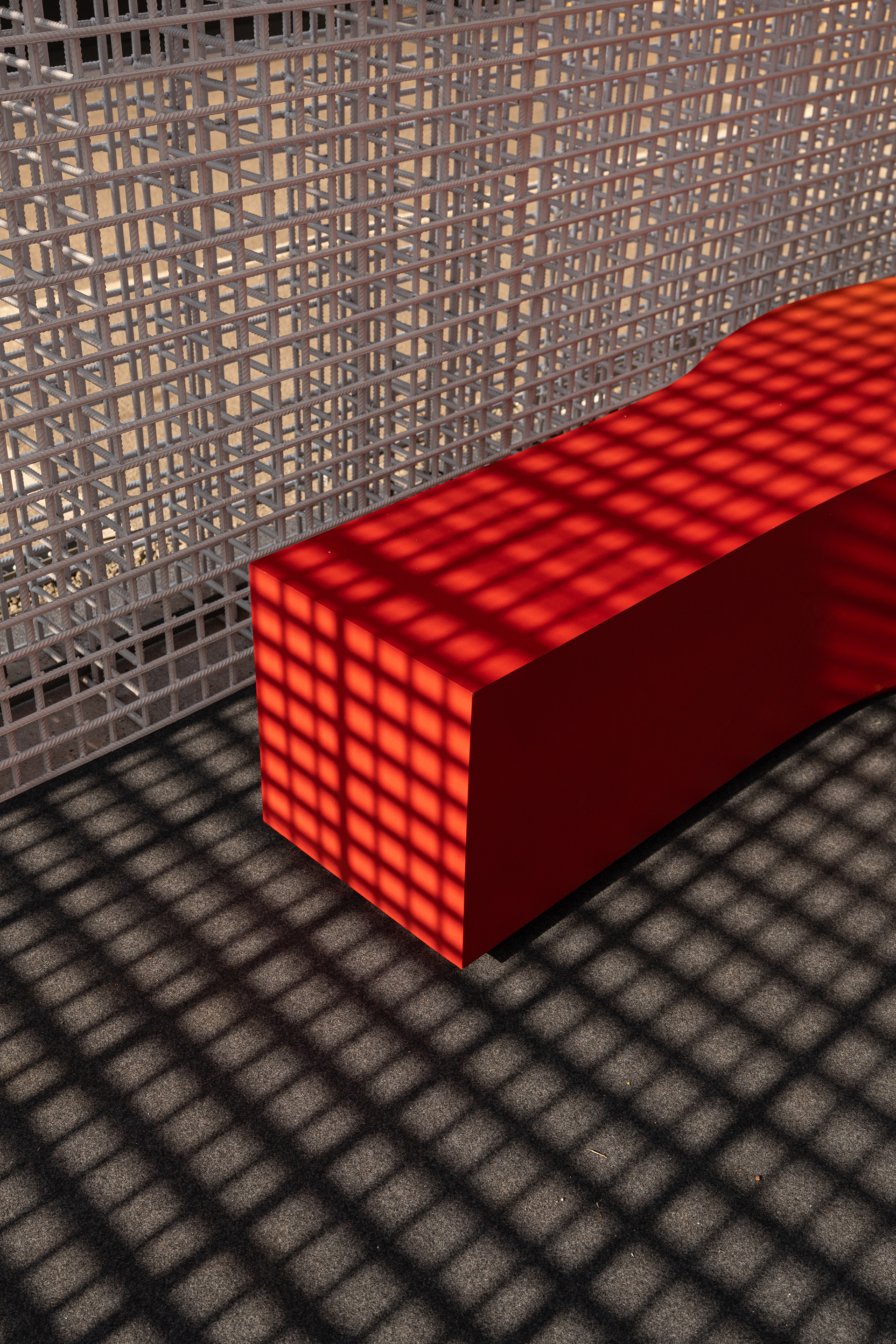 Red illuminated bench casting grid pattern shadows on textured floor near lattice wall