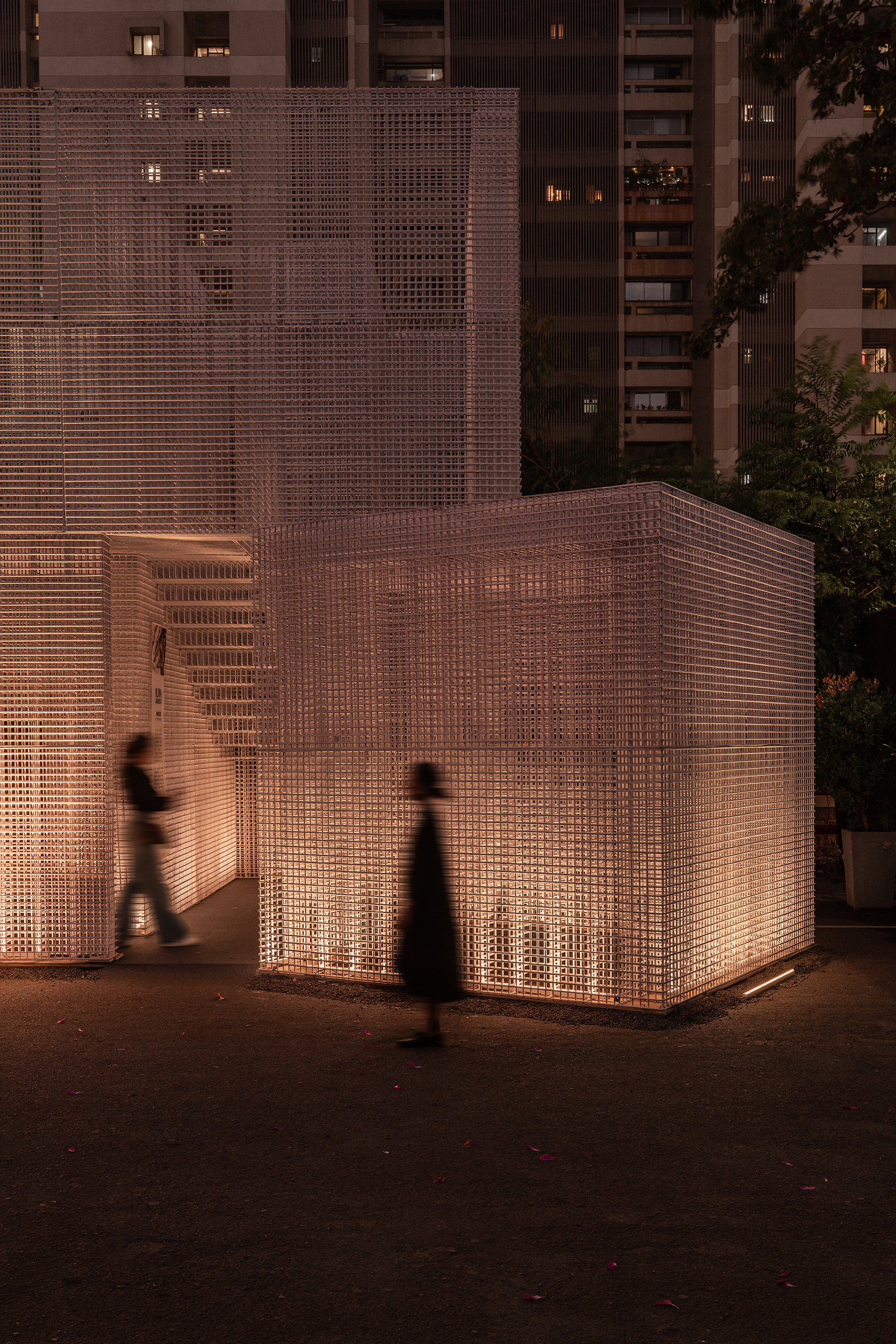 Close view of the perforated screen wall with interior staircase visible as figures pass at twilight