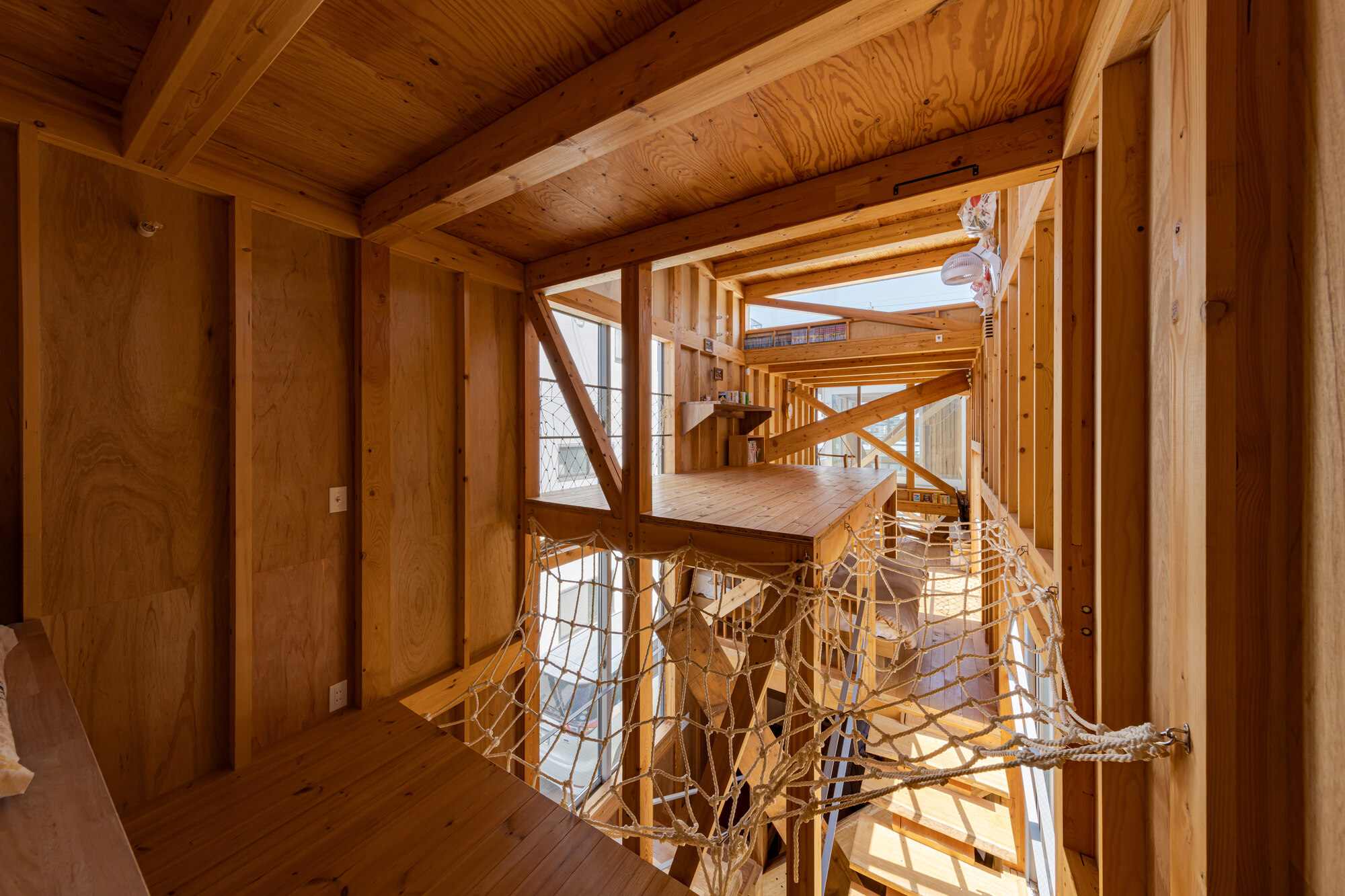 Interior view through timber-framed levels with rope net balustrade and exposed plywood ceiling