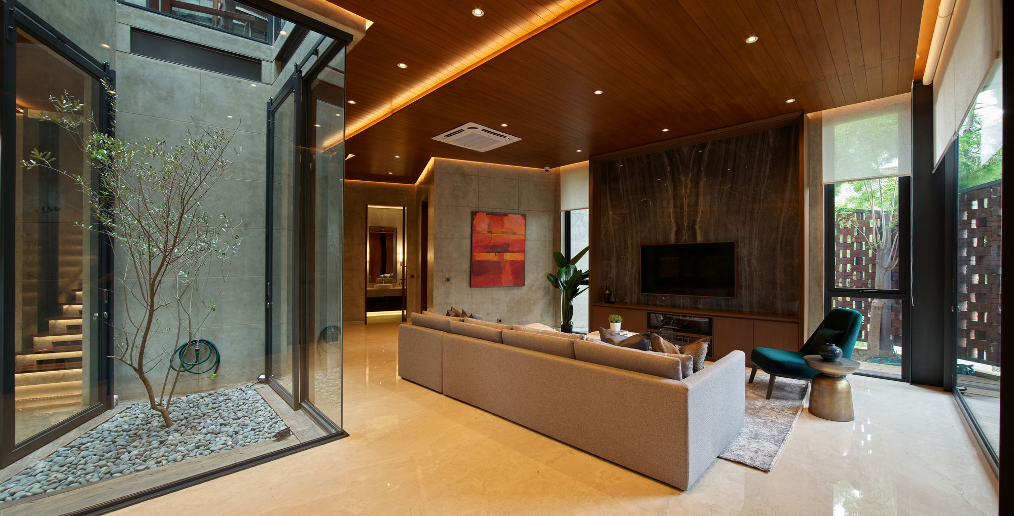 Living space with timber ceiling opening to two glazed courtyards with trees and stone flooring