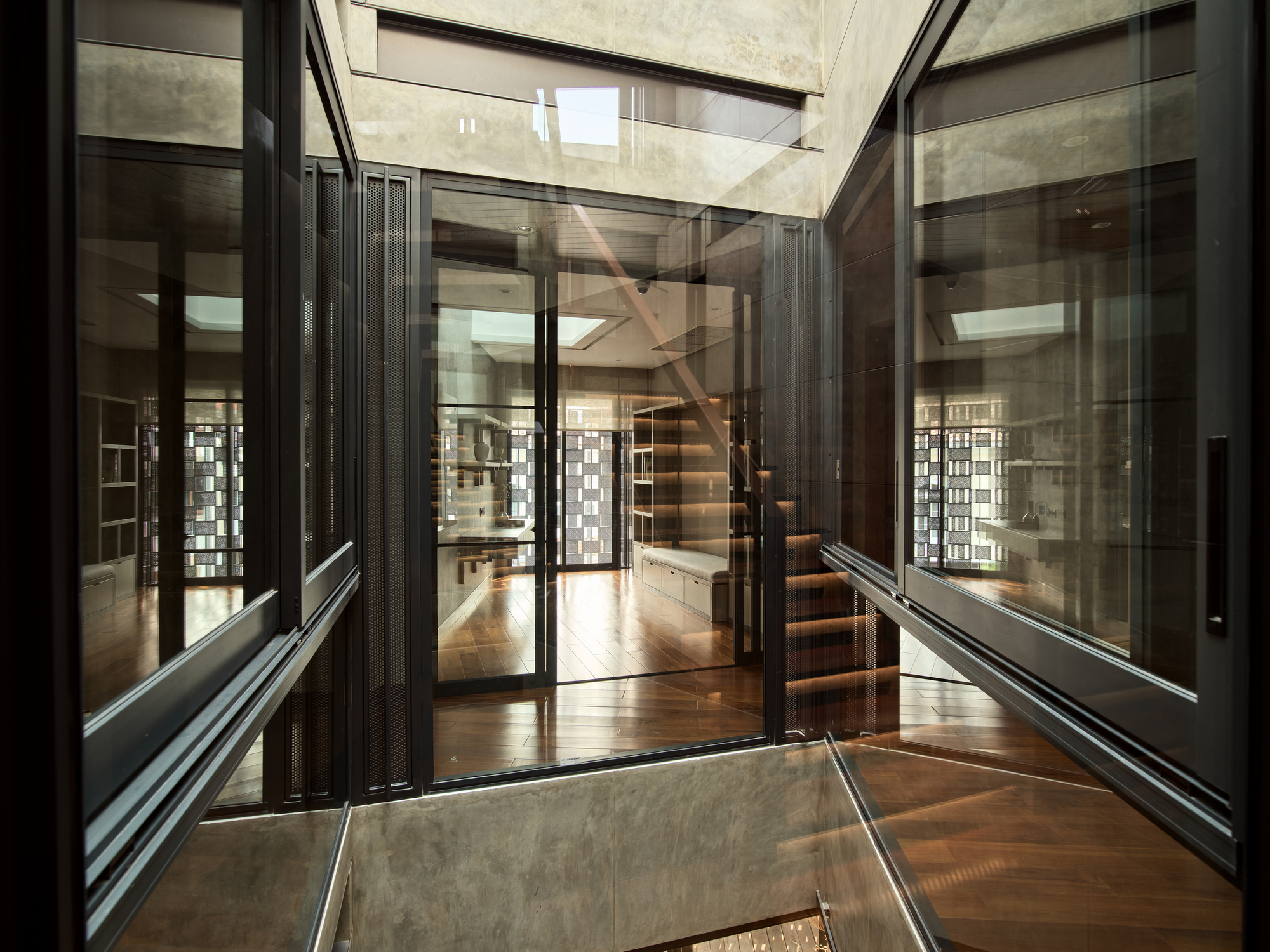Interior view through glass partitions showing a cantilevered timber staircase beneath a skylight