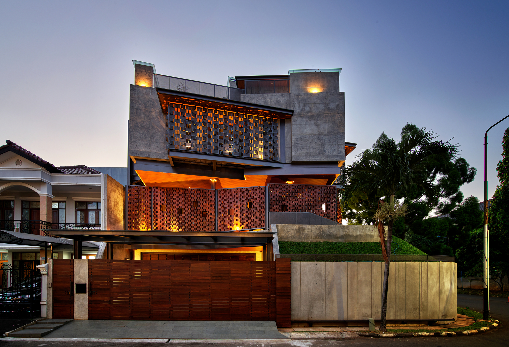 Street facade with perforated brick screens and concrete volumes illuminated from within at dusk