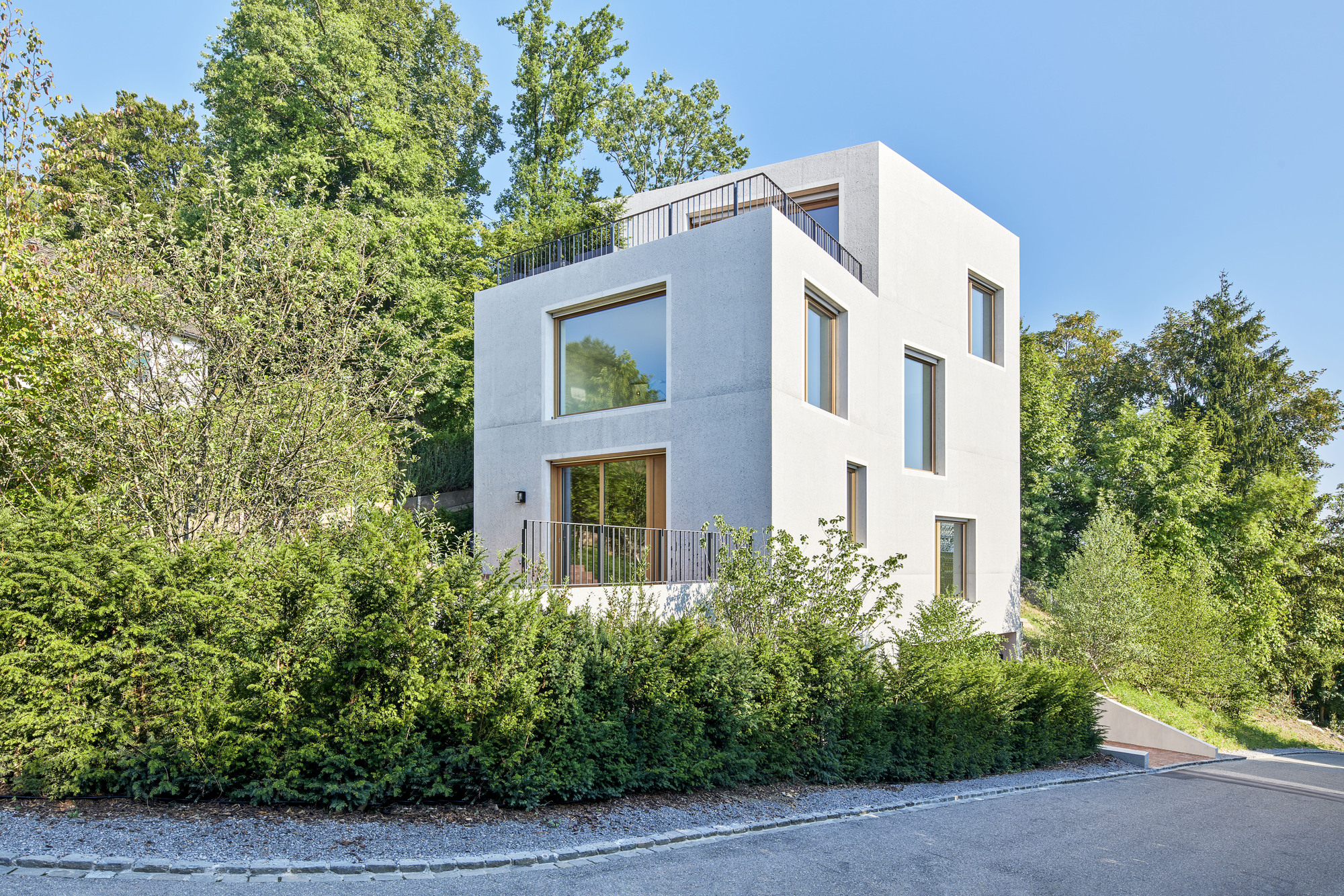 White rendered facade with stacked volumes and timber-framed windows surrounded by dense green foliage