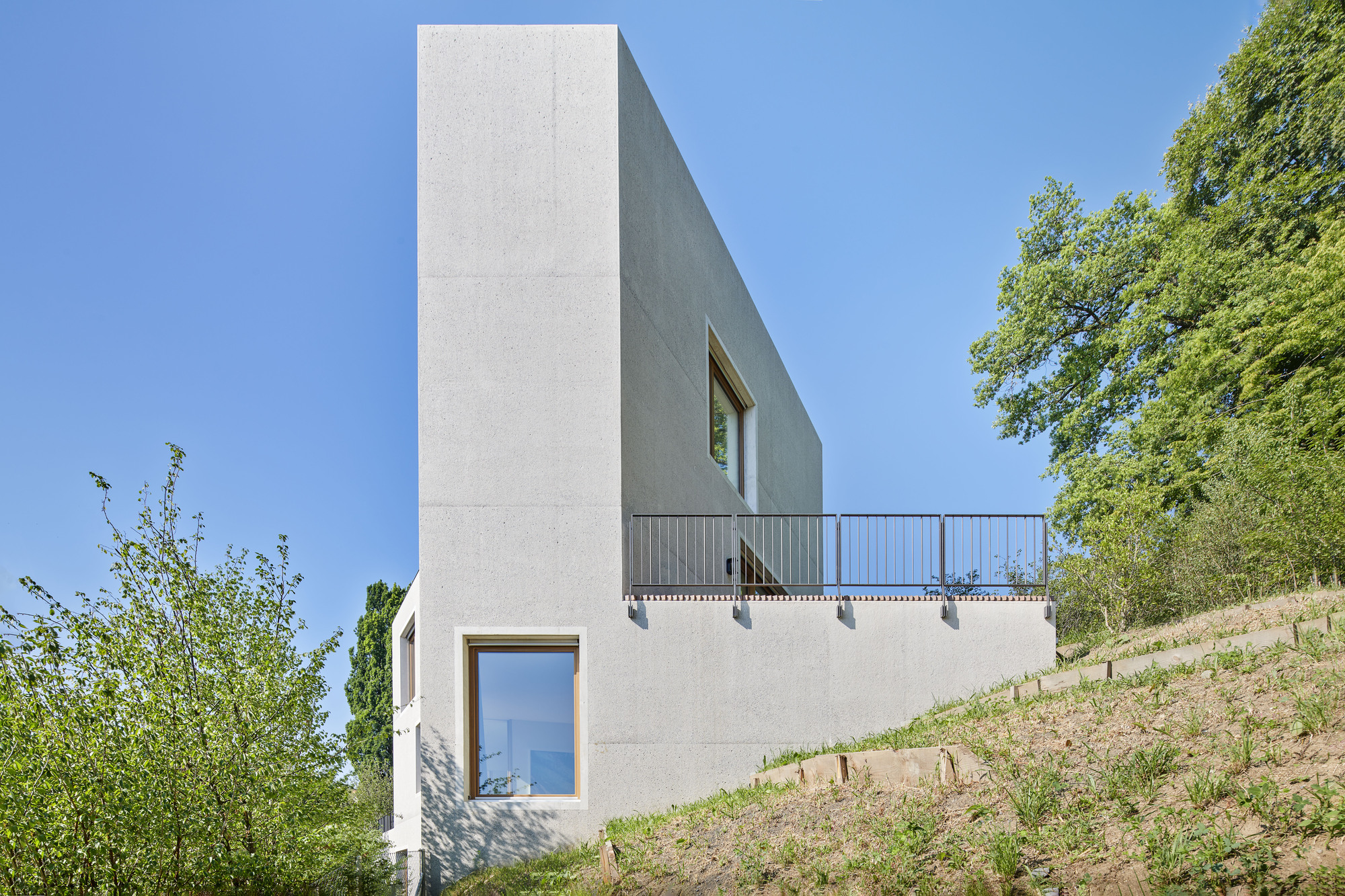 Side elevation showing punched window openings and a cantilevered terrace above terraced hillside plantings