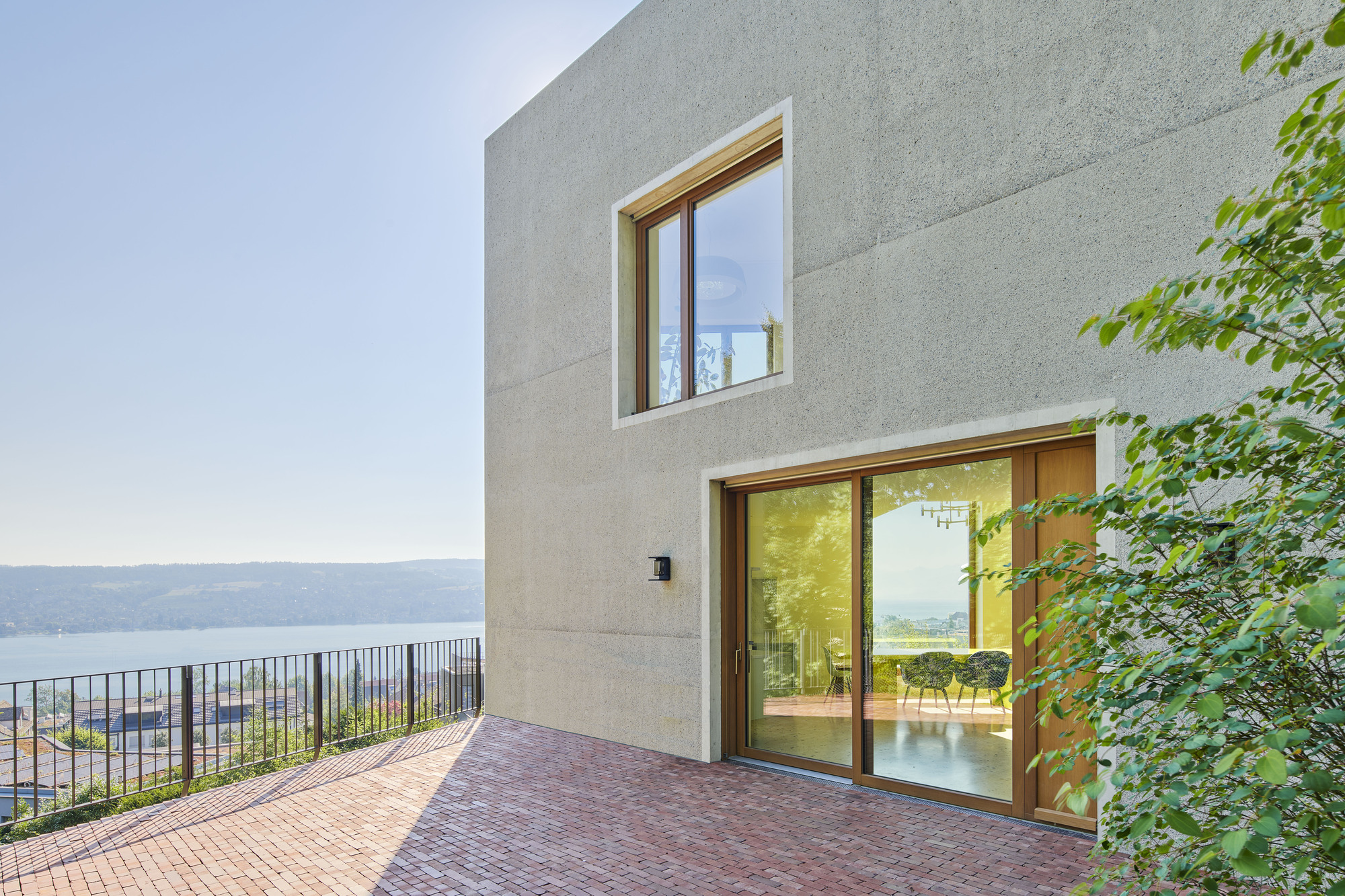 Brick paver terrace with timber-framed sliding doors opening to interior overlooking a distant lake under clear sky