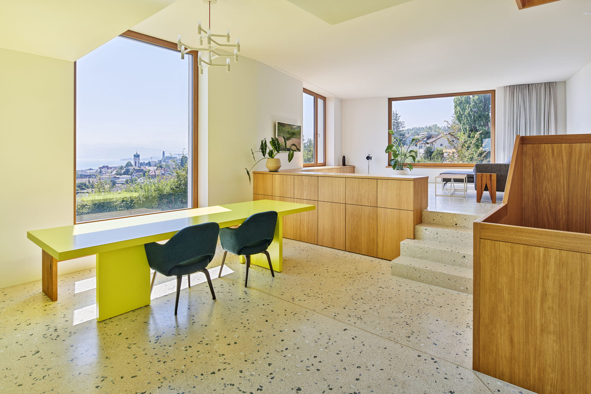 Split-level interior with terrazzo flooring, timber cabinetry, chartreuse table, and window framing distant cityscape