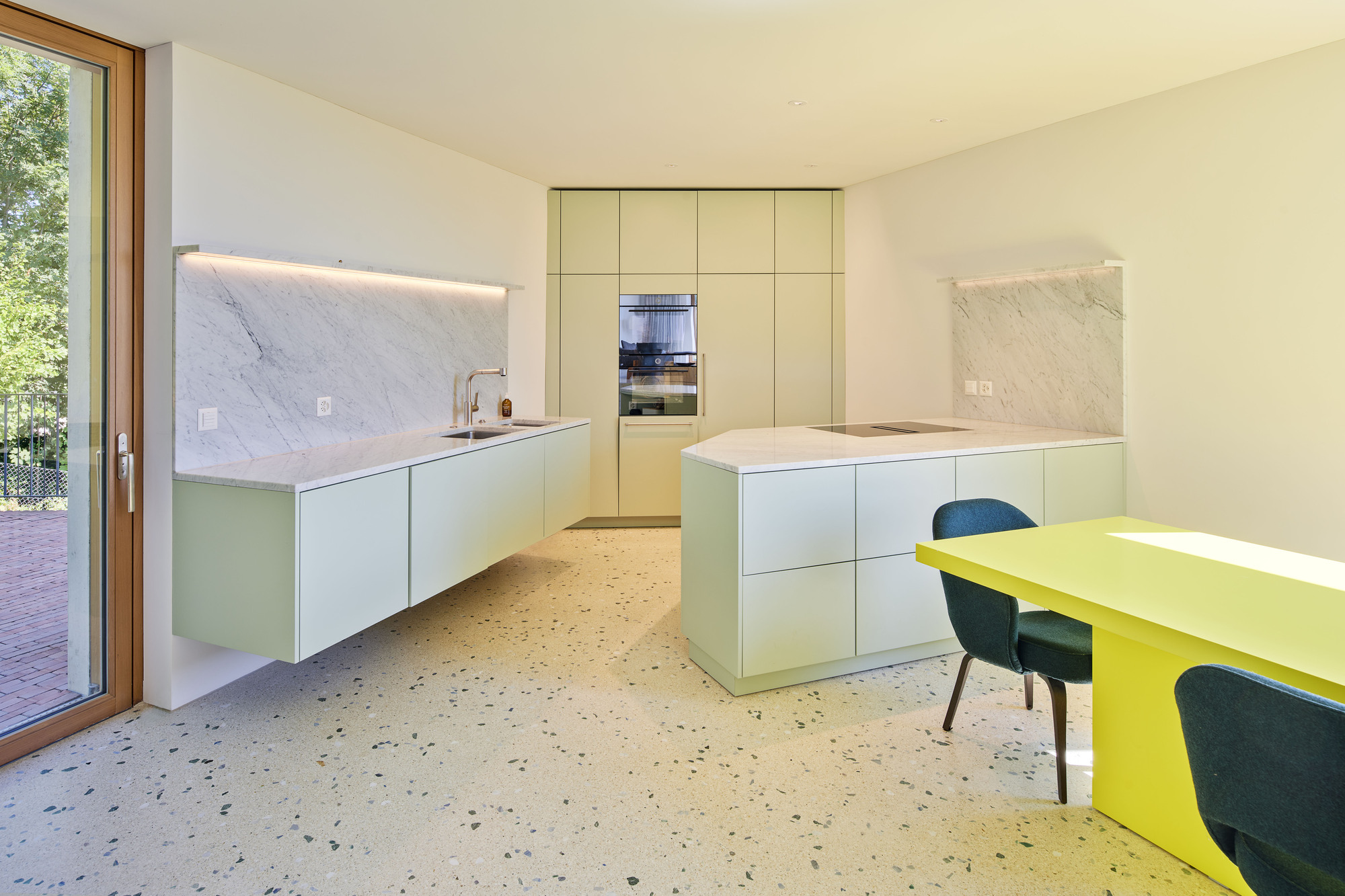Kitchen with floating pale green cabinetry, marble backsplash, terrazzo floor, and chartreuse dining table
